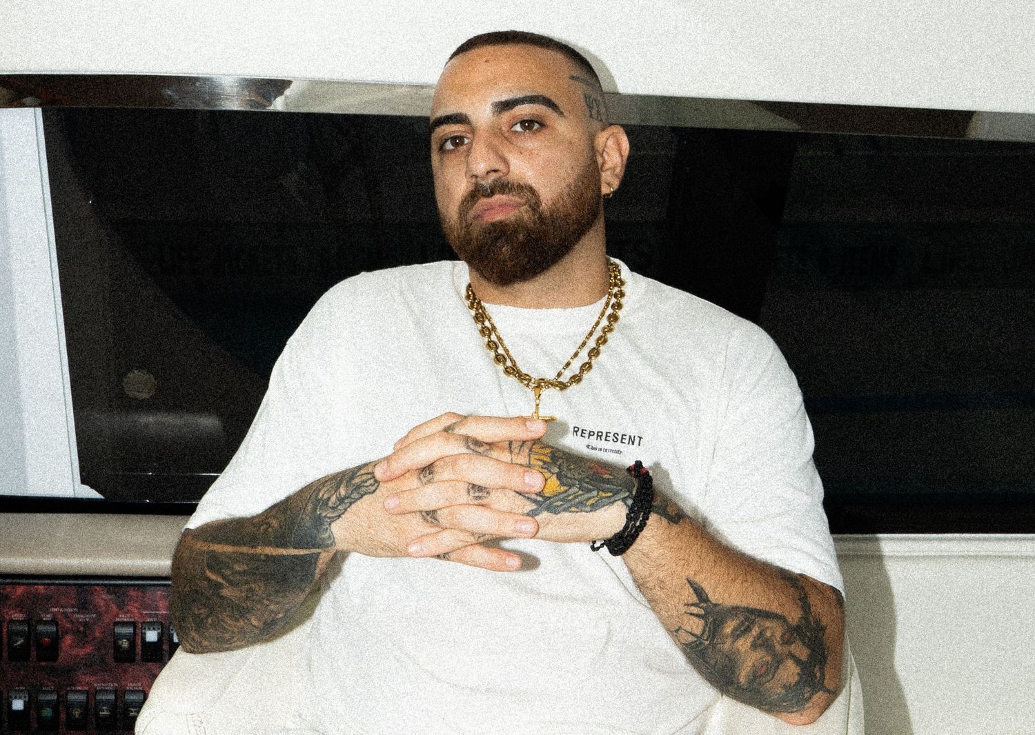 Tattooed man with gold chain necklace sitting casually in a studio setting.

portrait