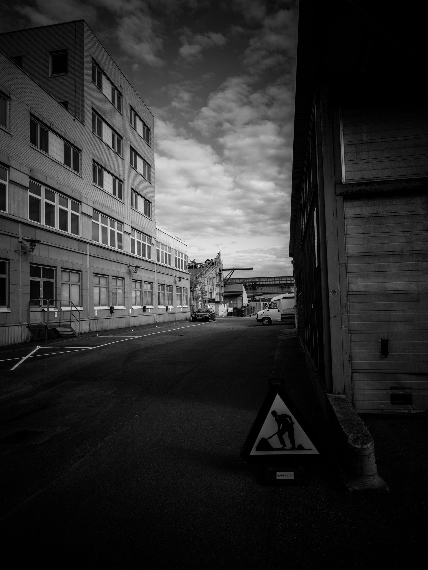 Dark urban street with construction warning sign beside an industrial building under cloudy sky.