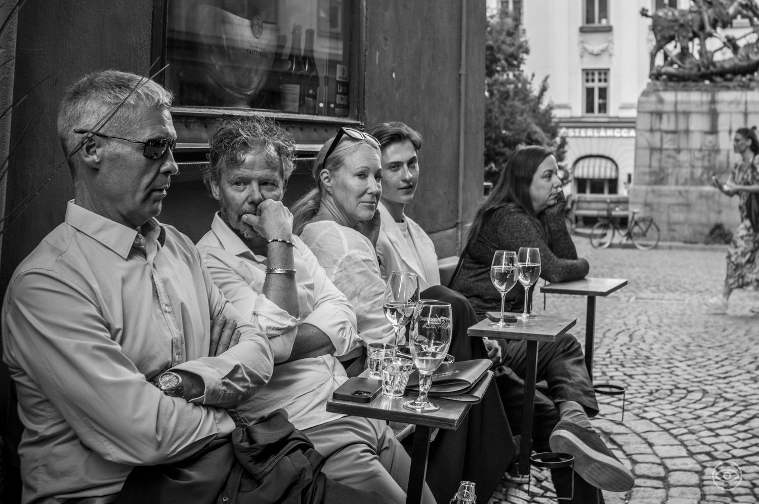 Group of people sitting at an outdoor cafe with wine glasses, black and white street photography.