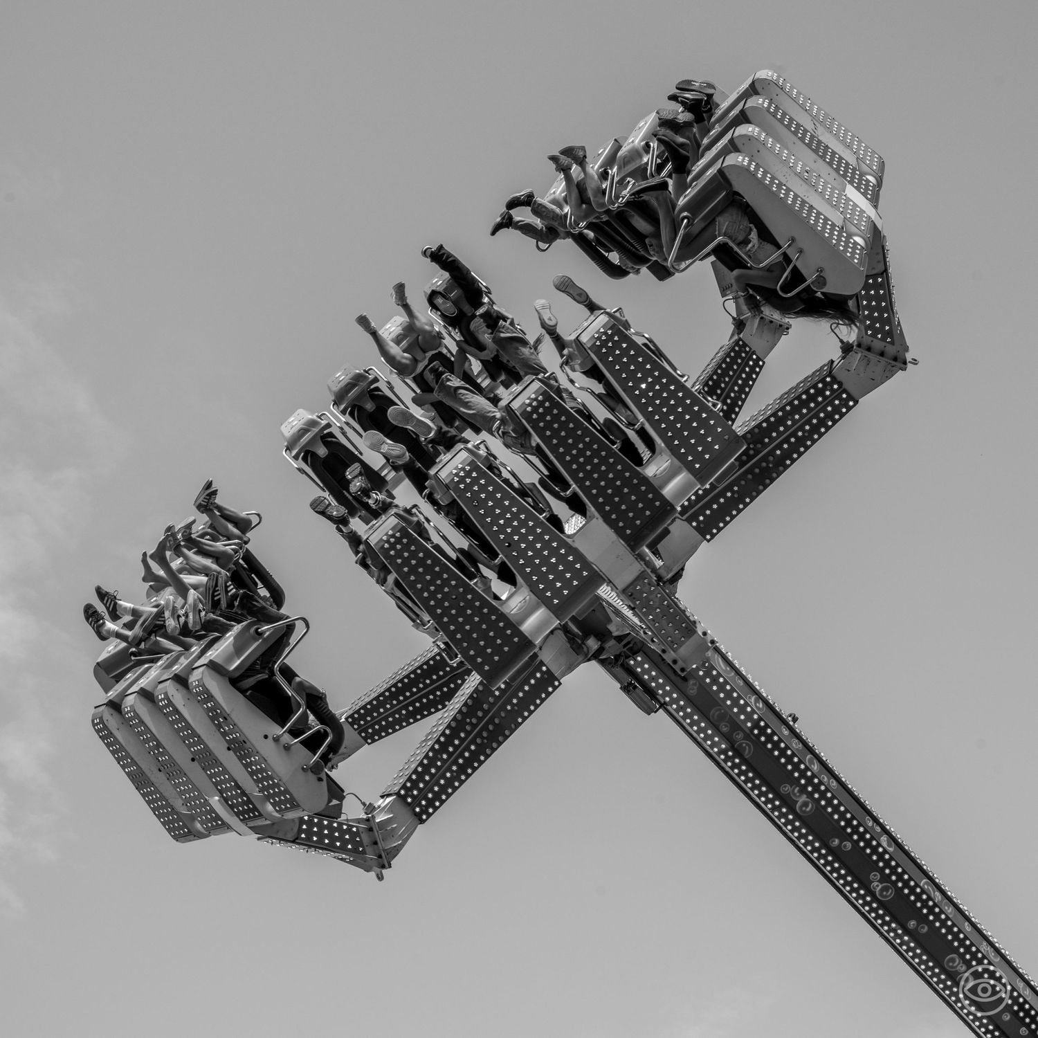 Black and white aerial view of riders on a thrilling inverted roller coaster against a grey sky.