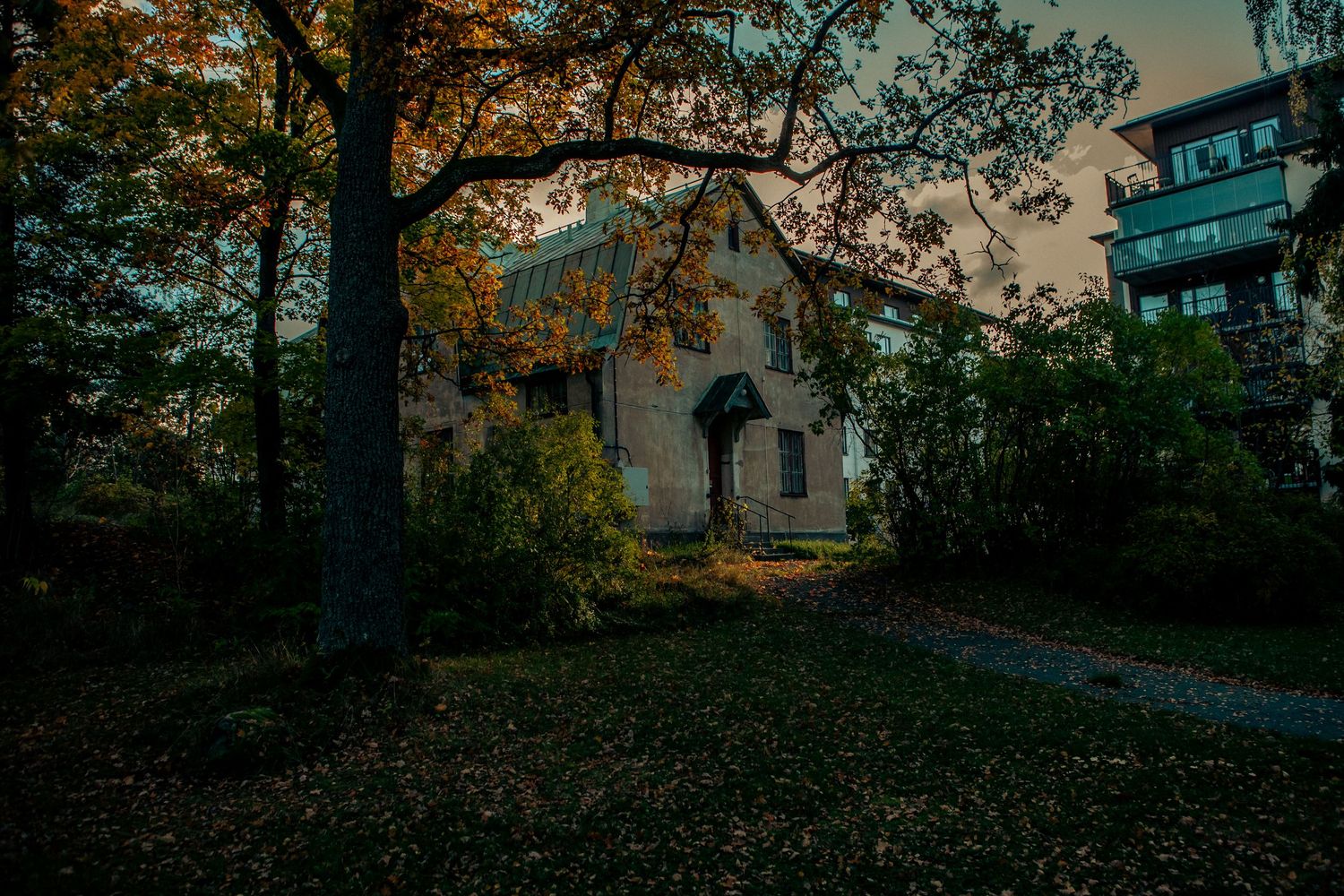 Historic stone church partially hidden by colorful autumn trees at dusk in a park.