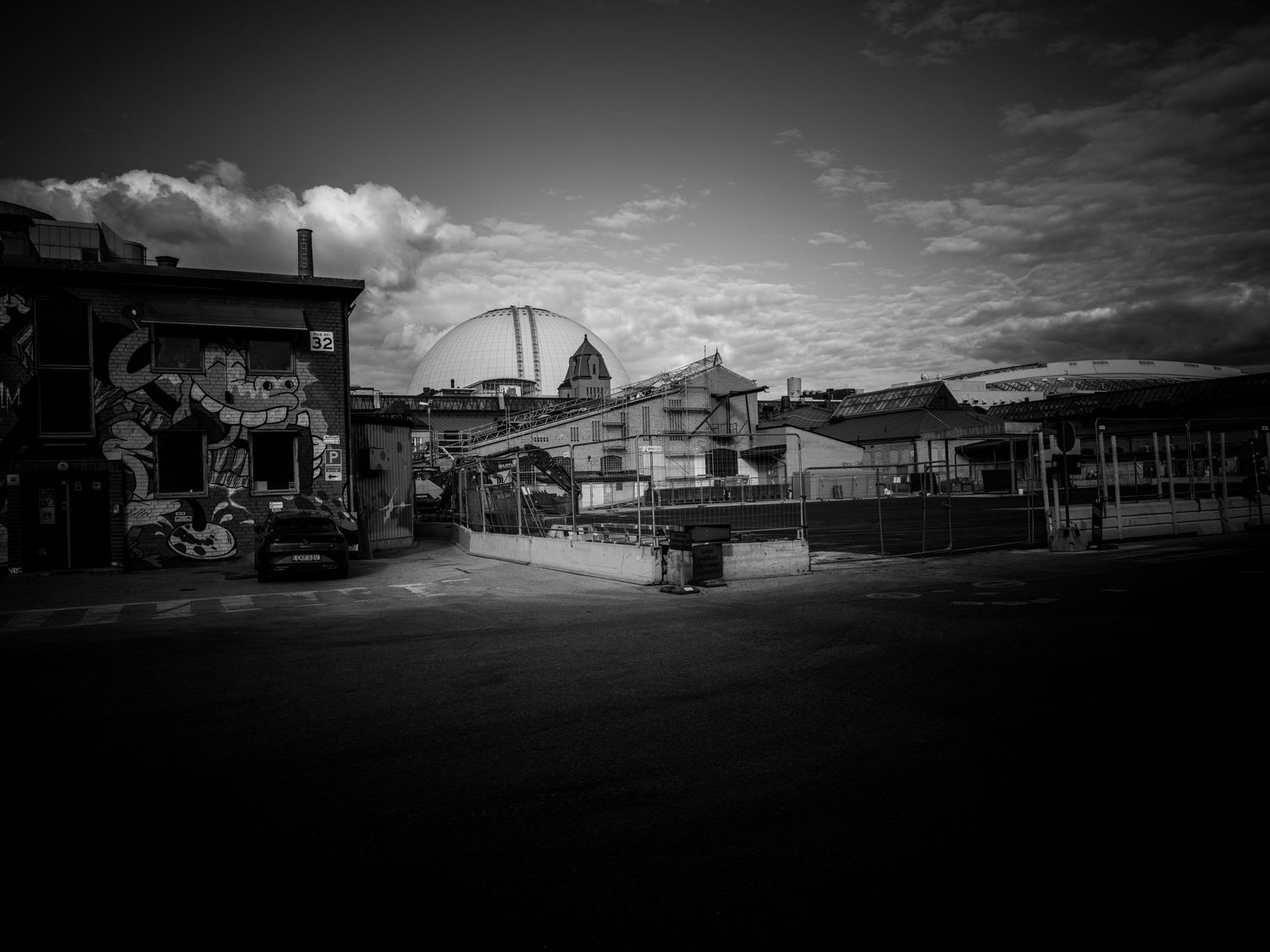 Black and white cityscape with street art, open plaza, and domed building under dramatic clouds.