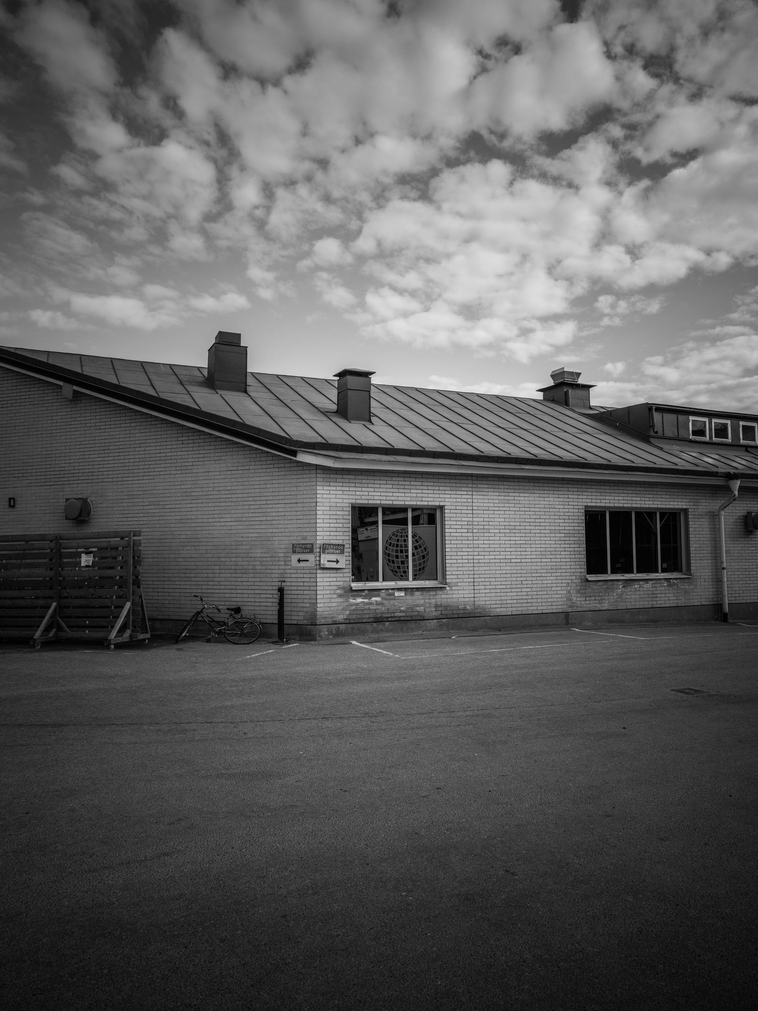 Black and white photo of a low brick building with metal roof under dramatic cloudy sky.