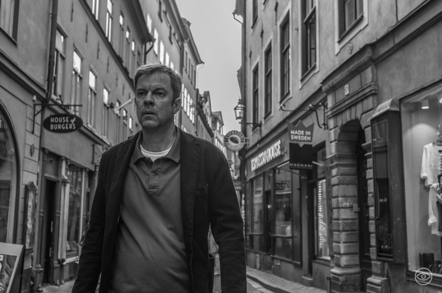 Middle-aged man in dark blazer walking through a narrow European old town street.