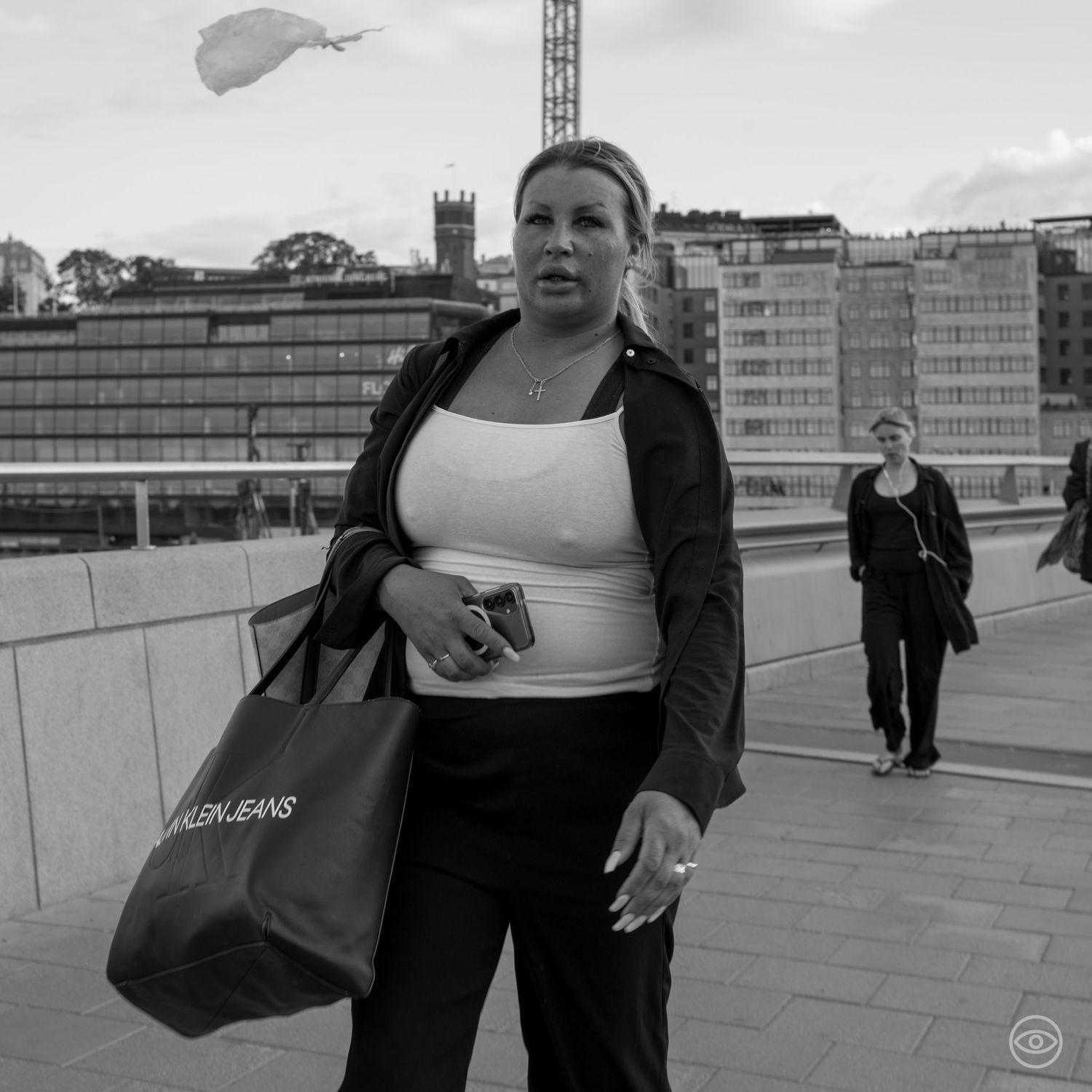 Woman carrying a Calvin Jeans bag walks along a waterfront promenade in black and white street photo.