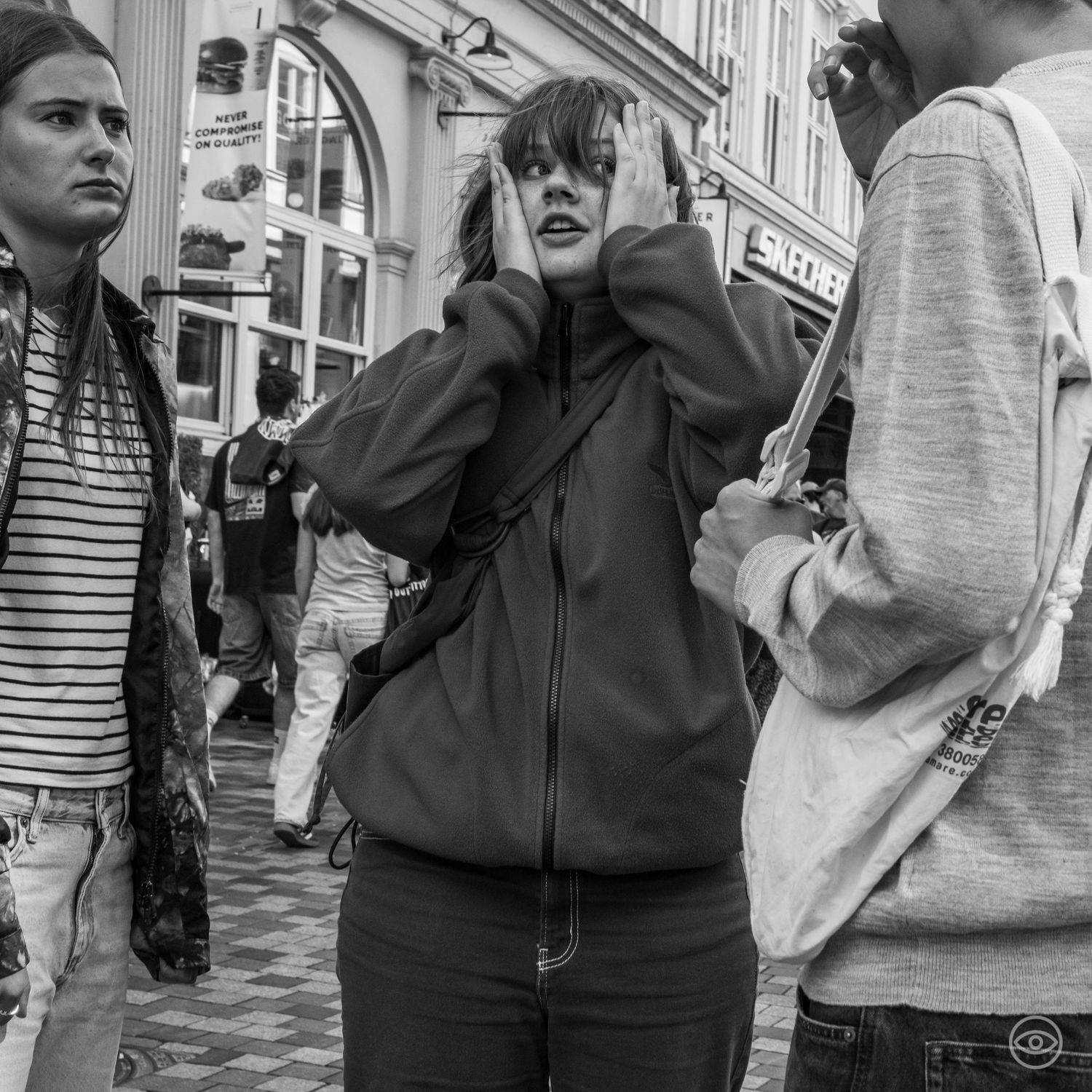 Young woman covering her ears with hands in a crowded urban street scene in black and white.