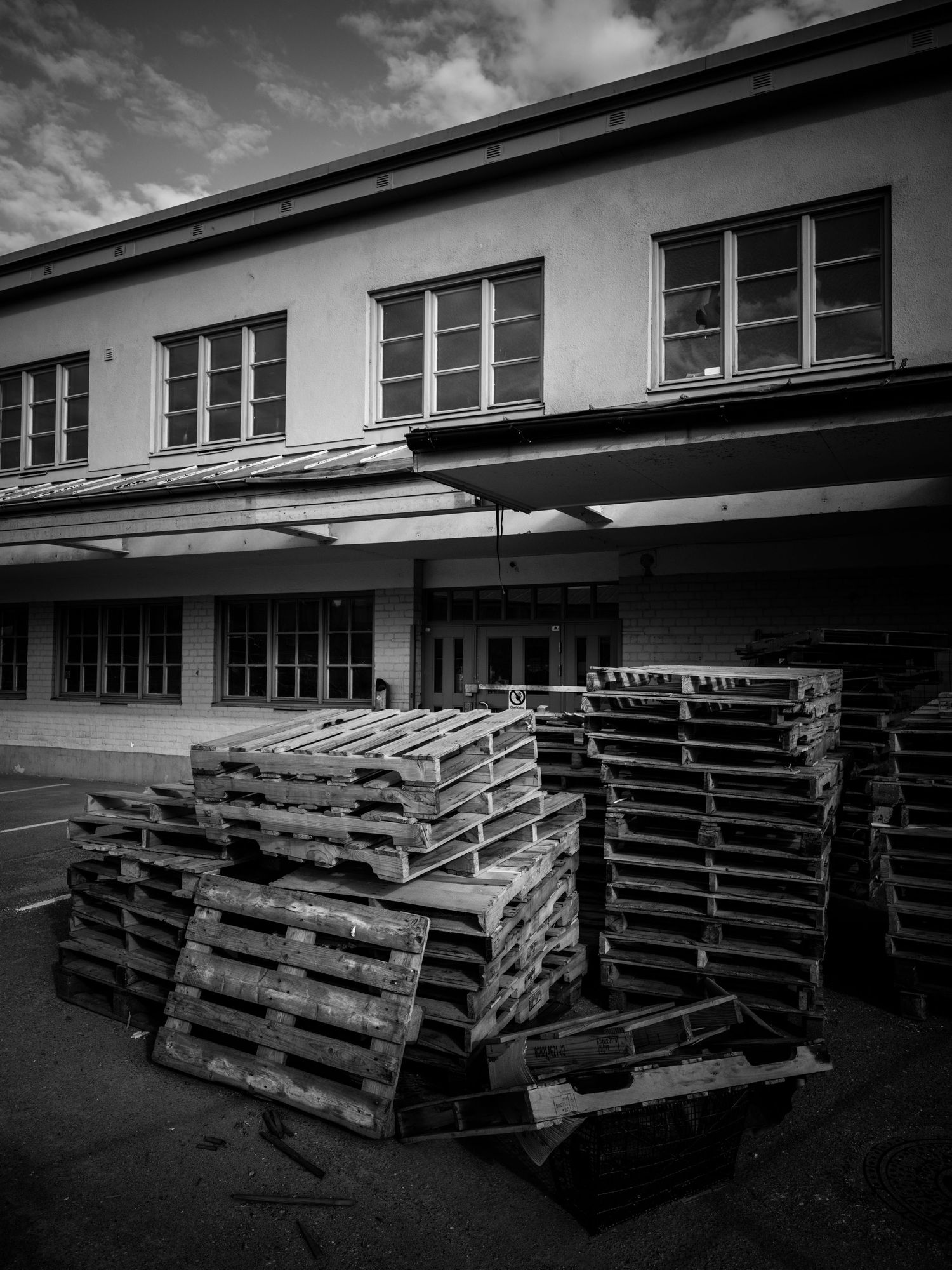 Stacked wooden pallets piled outside an old industrial building in black and white.