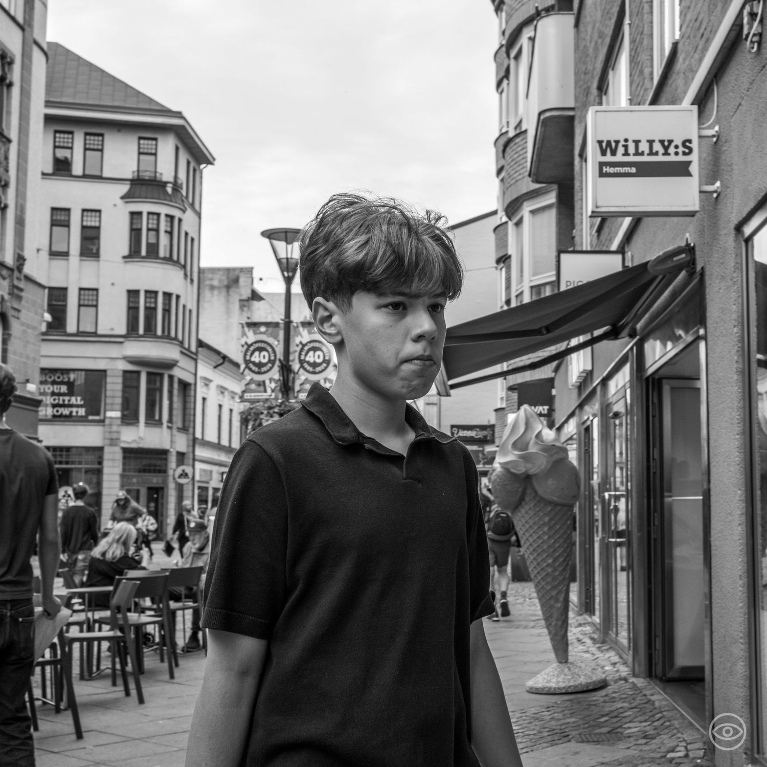 Young boy holding an ice cream cone stands on a cobblestone street near a Willy's shop in black and white.