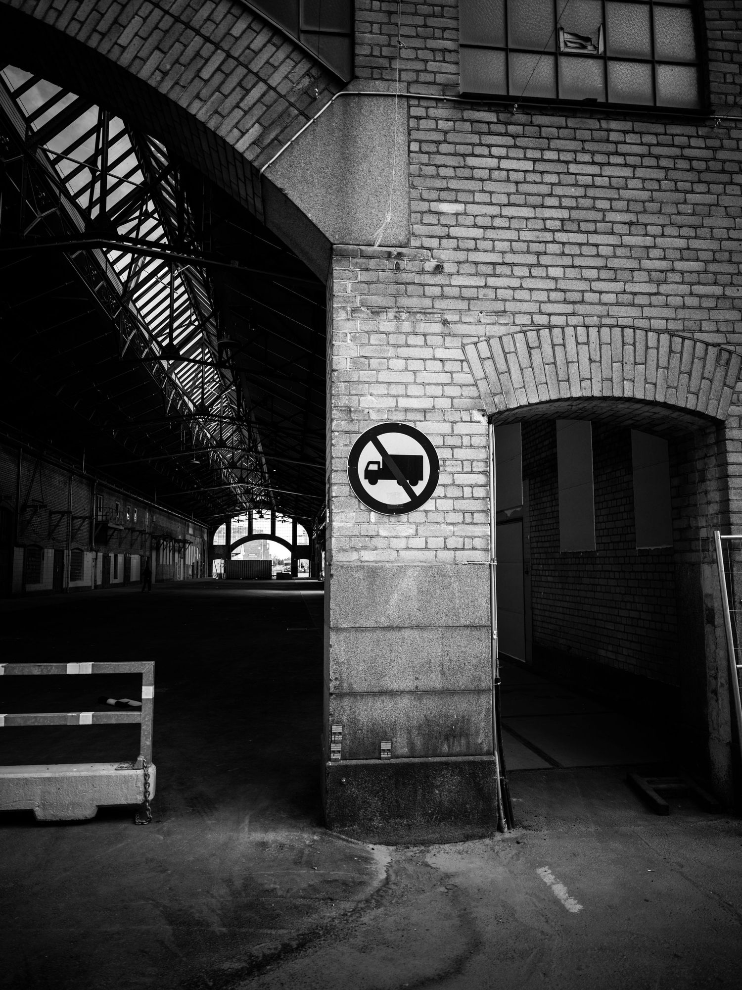 No trucks sign on a brick pillar inside a dark abandoned industrial building interior.