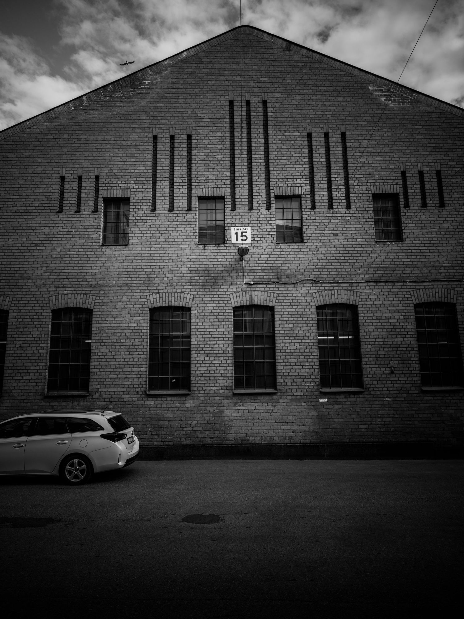 Brick industrial building facade with number 15 sign and parked white car below.