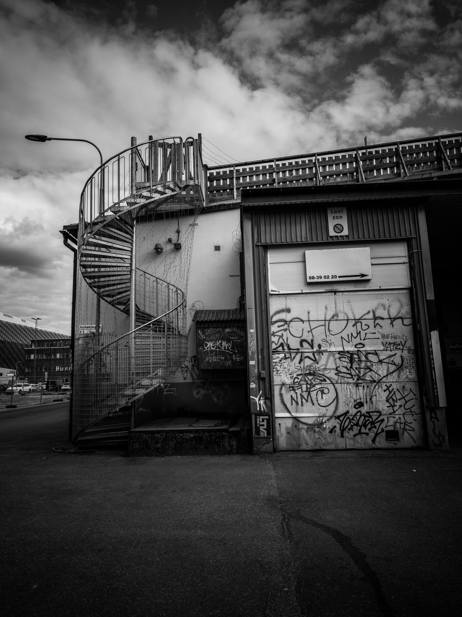 Black and white photo of a spiral staircase on a graffiti-covered industrial building.
