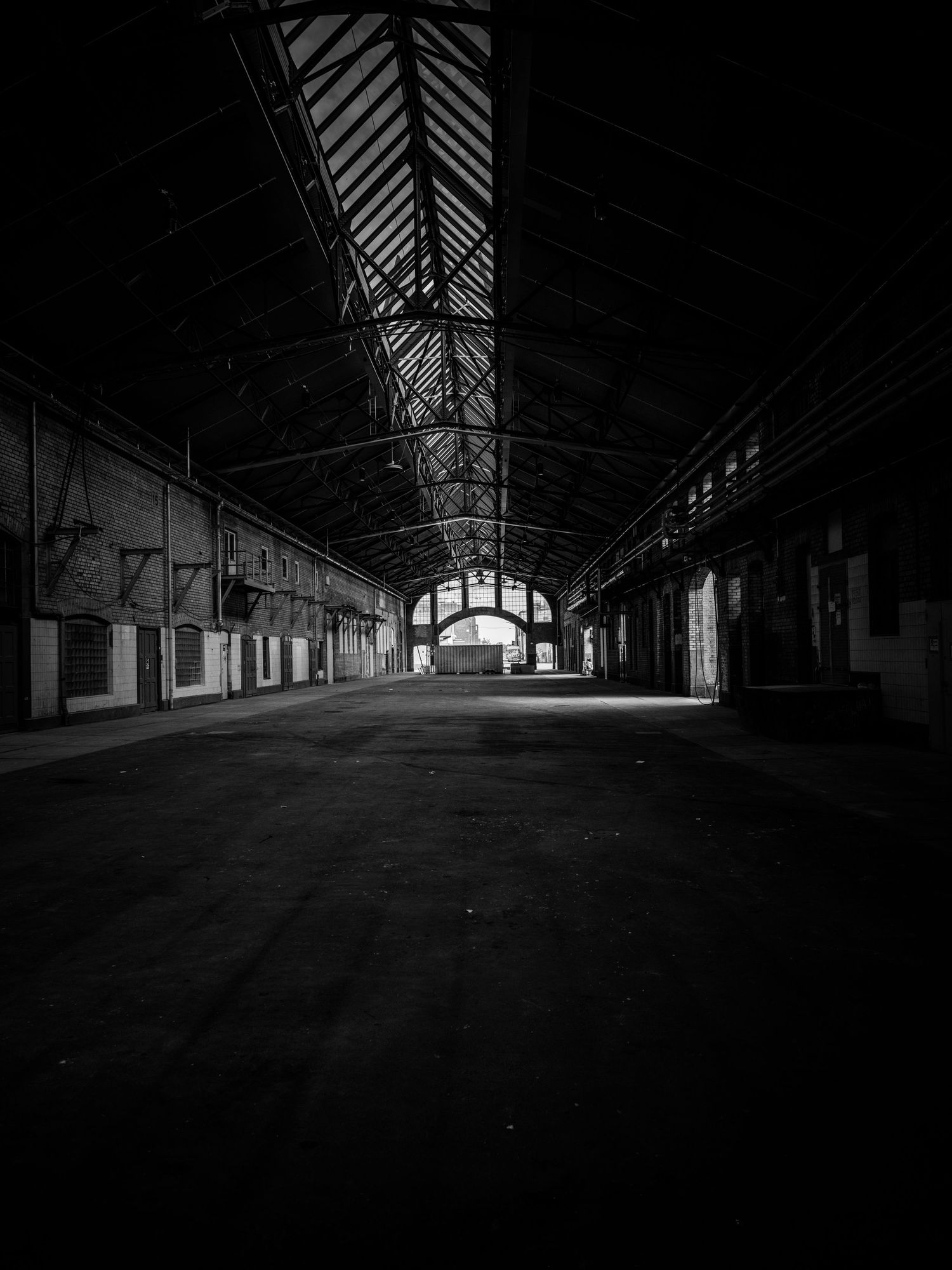 Empty abandoned warehouse interior with iron roof structure and light at the end.