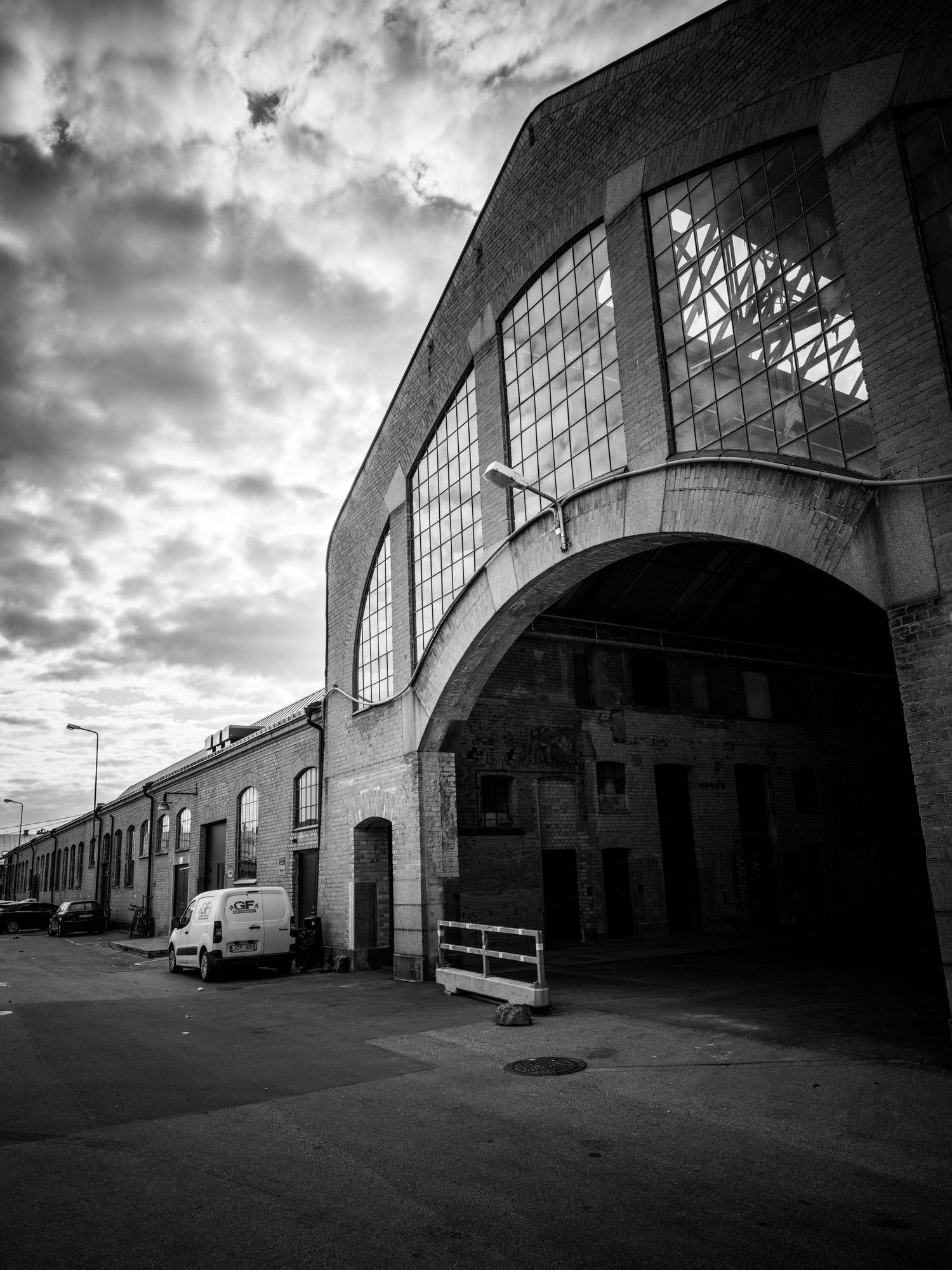 Black and white photo of a curved brick warehouse with large arched windows under cloudy sky.