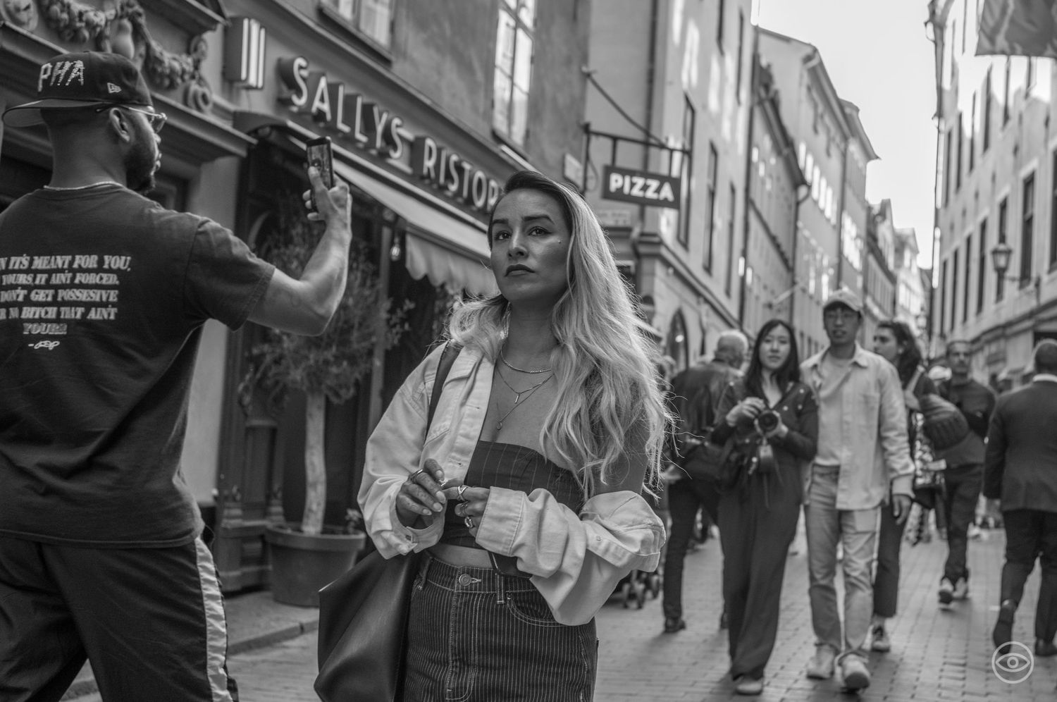 Young blonde woman in denim jacket walking on a busy urban shopping street.