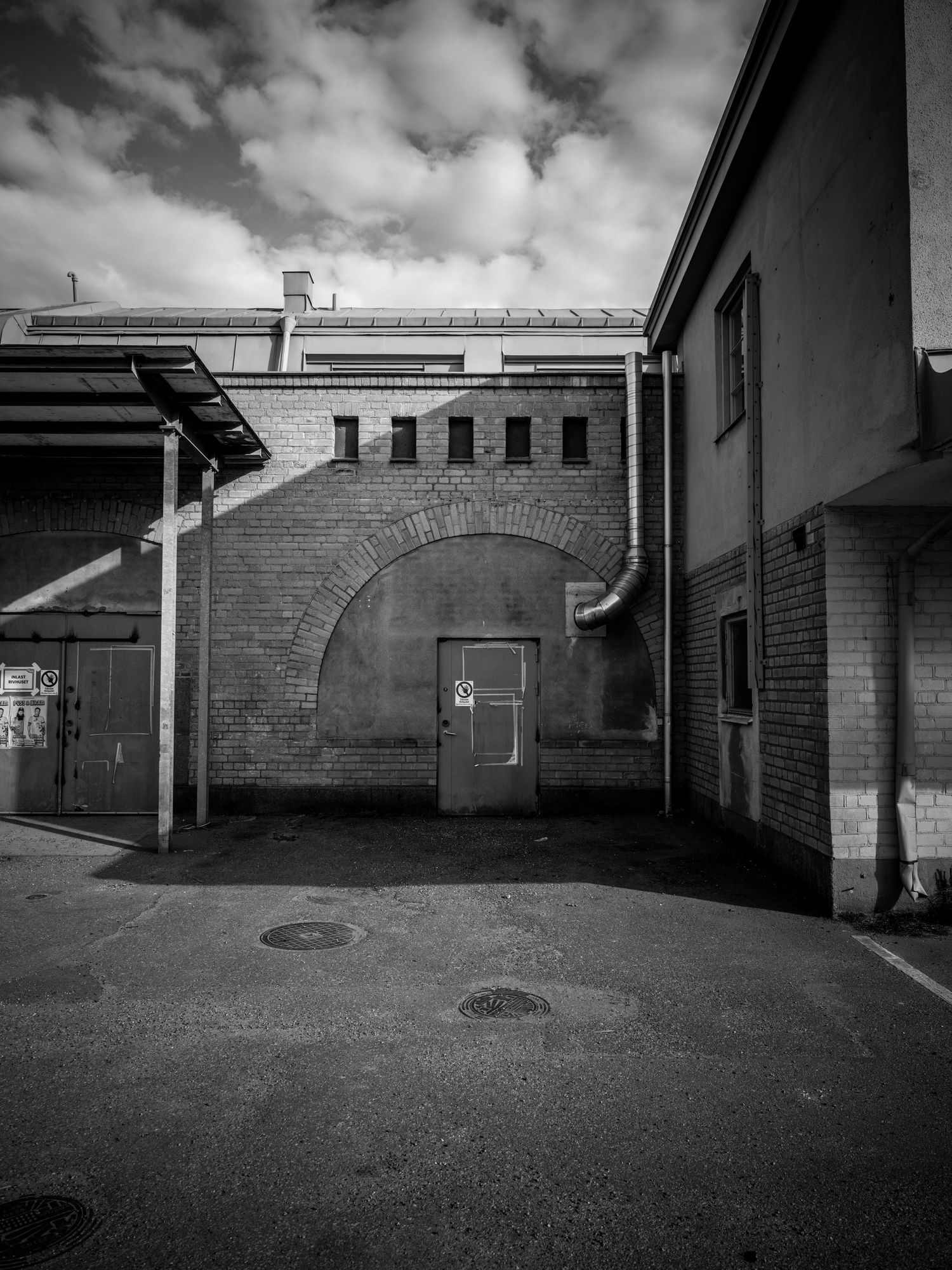 Black and white photo of a brick industrial building with arched wall and metal door.