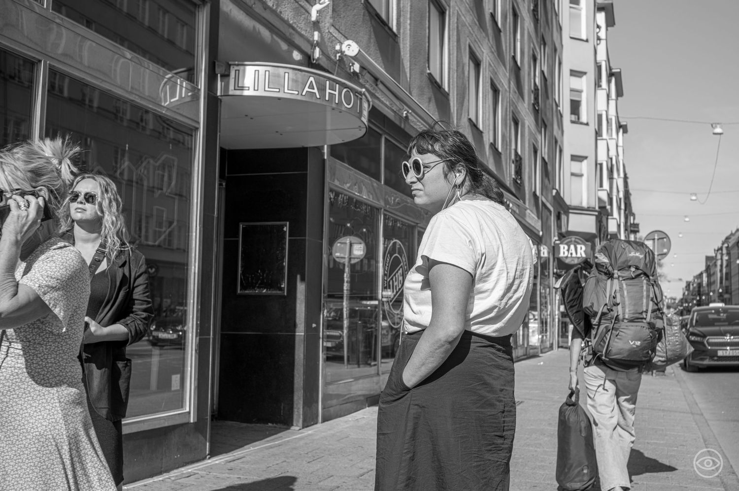 Two women stand outside the Lilla Hotel entrance on a sunny urban street in black and white photography.