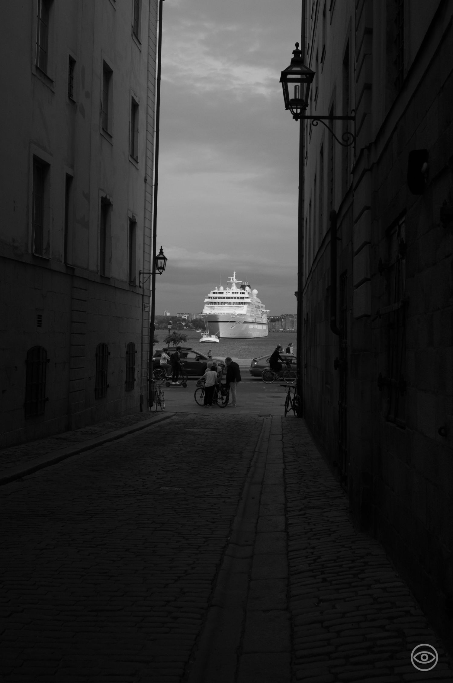 Narrow cobblestone alley frames a large cruise ship docked at harbor in black and white photography.
