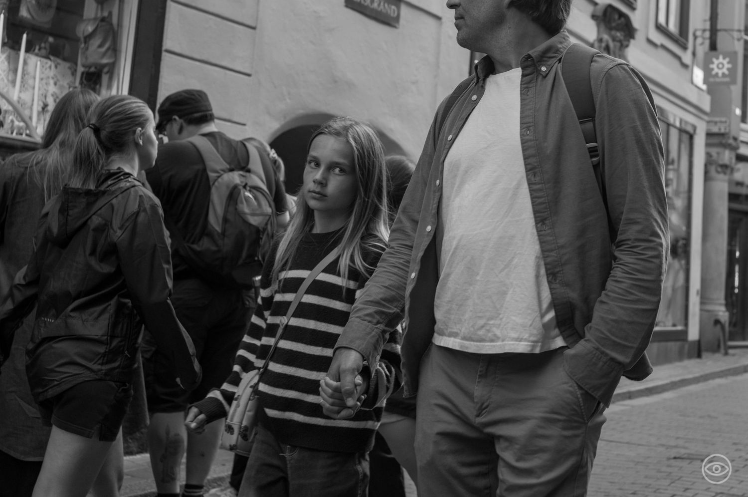 Young girl in striped shirt holding hands with an adult on a busy city street.