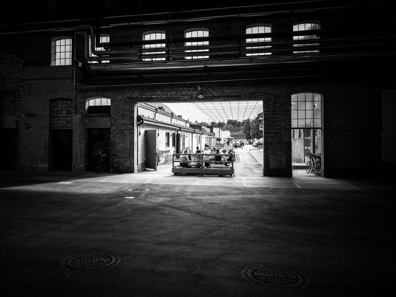 Black and white photo framing a sunlit courtyard through a dark industrial brick archway.