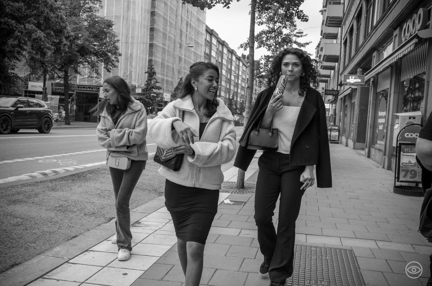 Three young women walking together on a city sidewalk in black and white street photography.