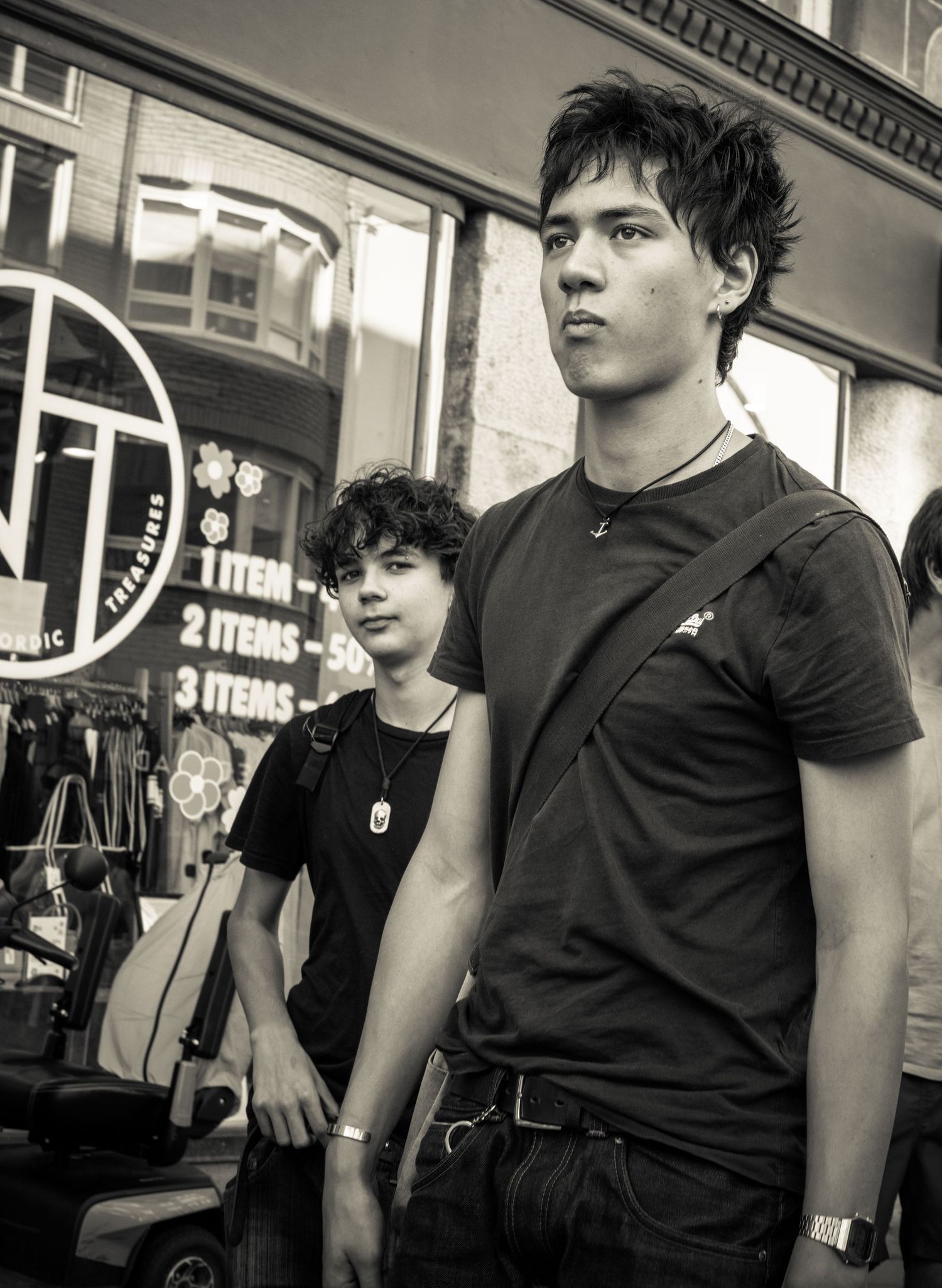 Two young people in black t-shirts stand outside urban thrift store in black and white photo.
