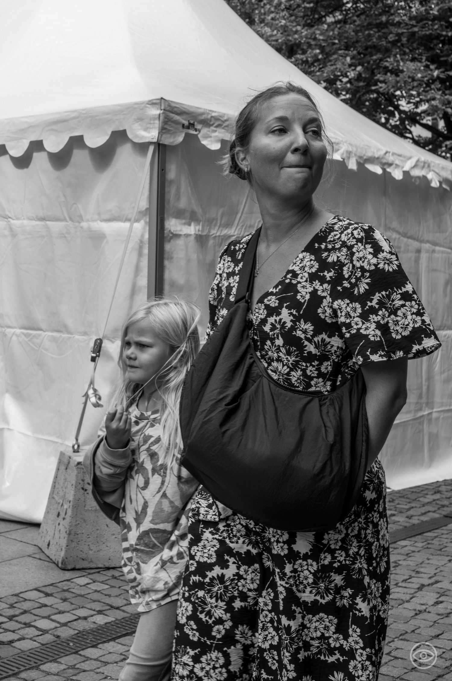 Mother in floral dress with young blonde daughter standing near a white tent in black and white.