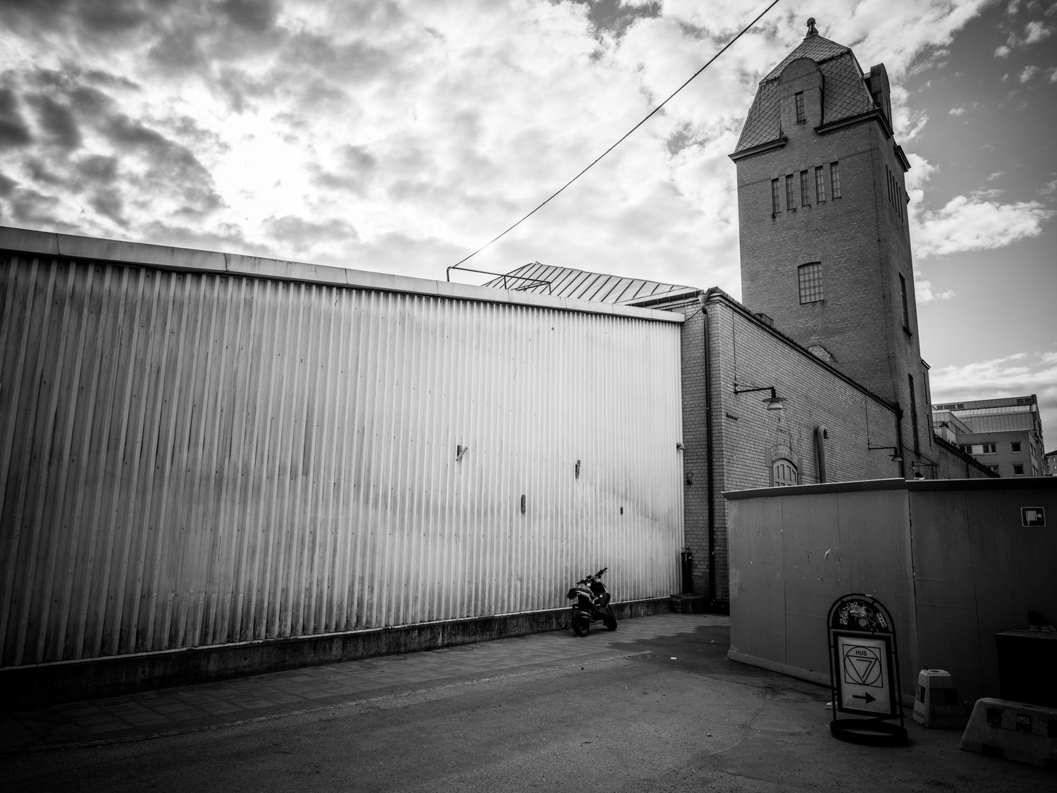 Black and white urban photo of corrugated metal wall with a historic tower in the background.