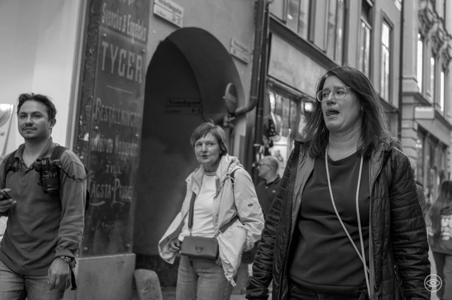 Three people walking on a city street, woman in foreground wearing glasses and earphones.