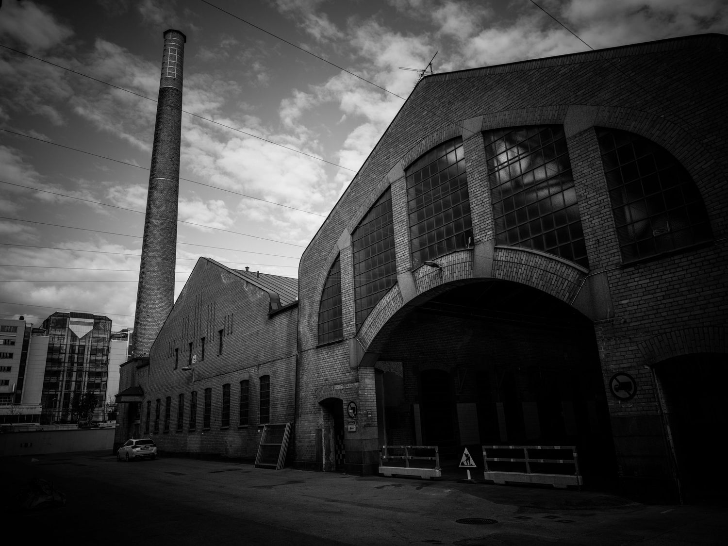 Black and white photo of a large brick industrial building with tall chimney and arched entrance.