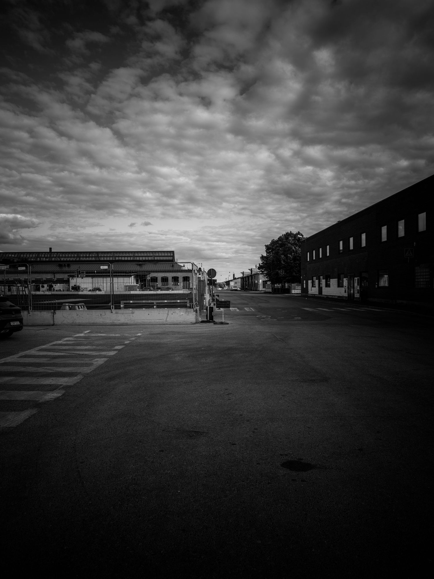 Black and white photo of an empty industrial parking lot with a barrier gate and cloudy sky.
