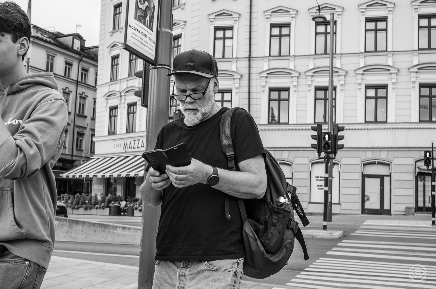 Middle-aged man in black cap and t-shirt checks his phone on a city street in black and white photography.