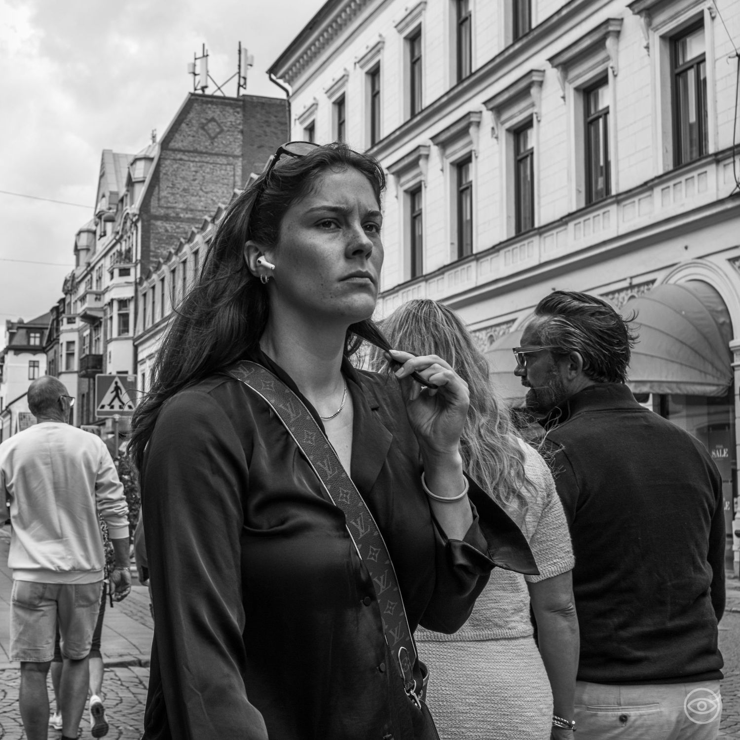 Young woman with dark hair and earbuds walks through a European city street in black and white photography.