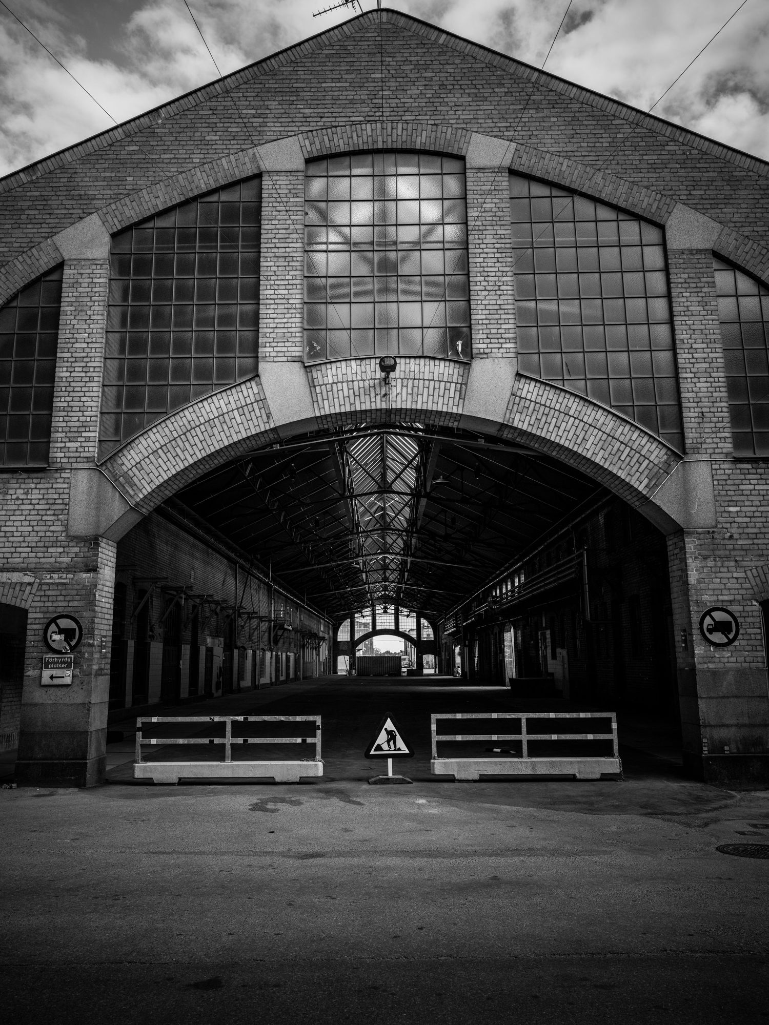 Entrance to an abandoned brick industrial hall with arched windows and warning signs.