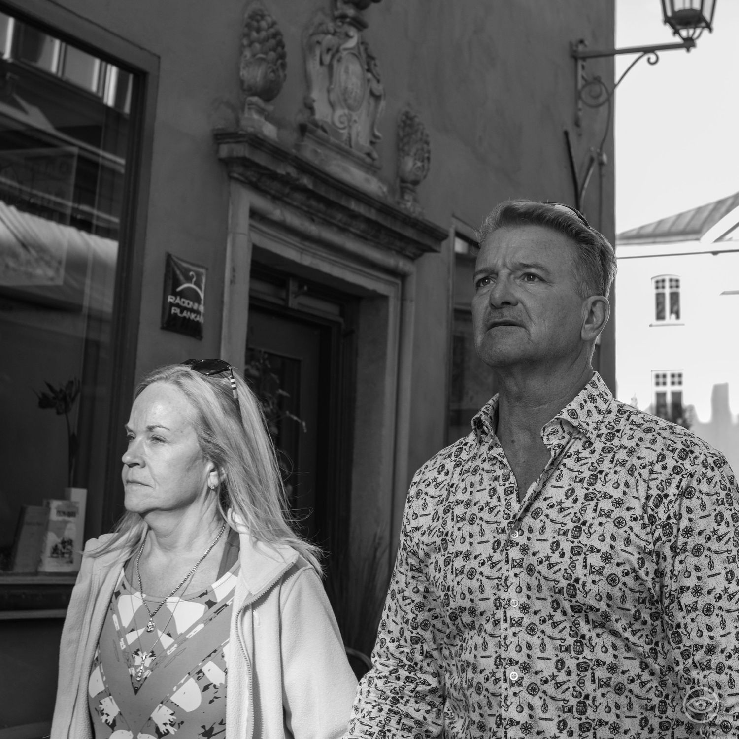 Blonde woman and tall man in floral shirt standing outside a historic building.