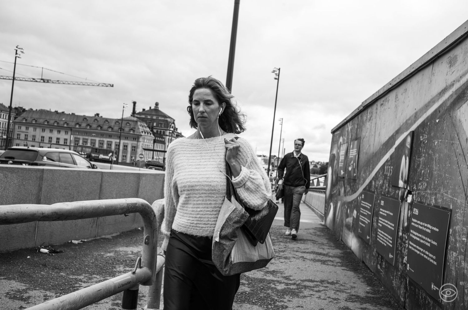 Woman carrying a handbag walking on a urban bridge pathway, black and white street photography.
