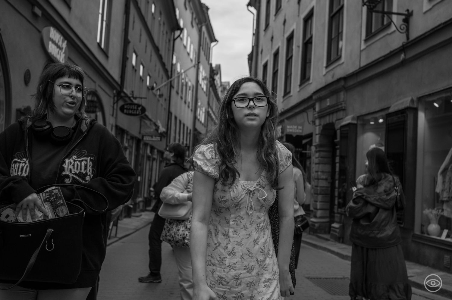 Young woman in a floral dress walks through a narrow European city street in black and white.
