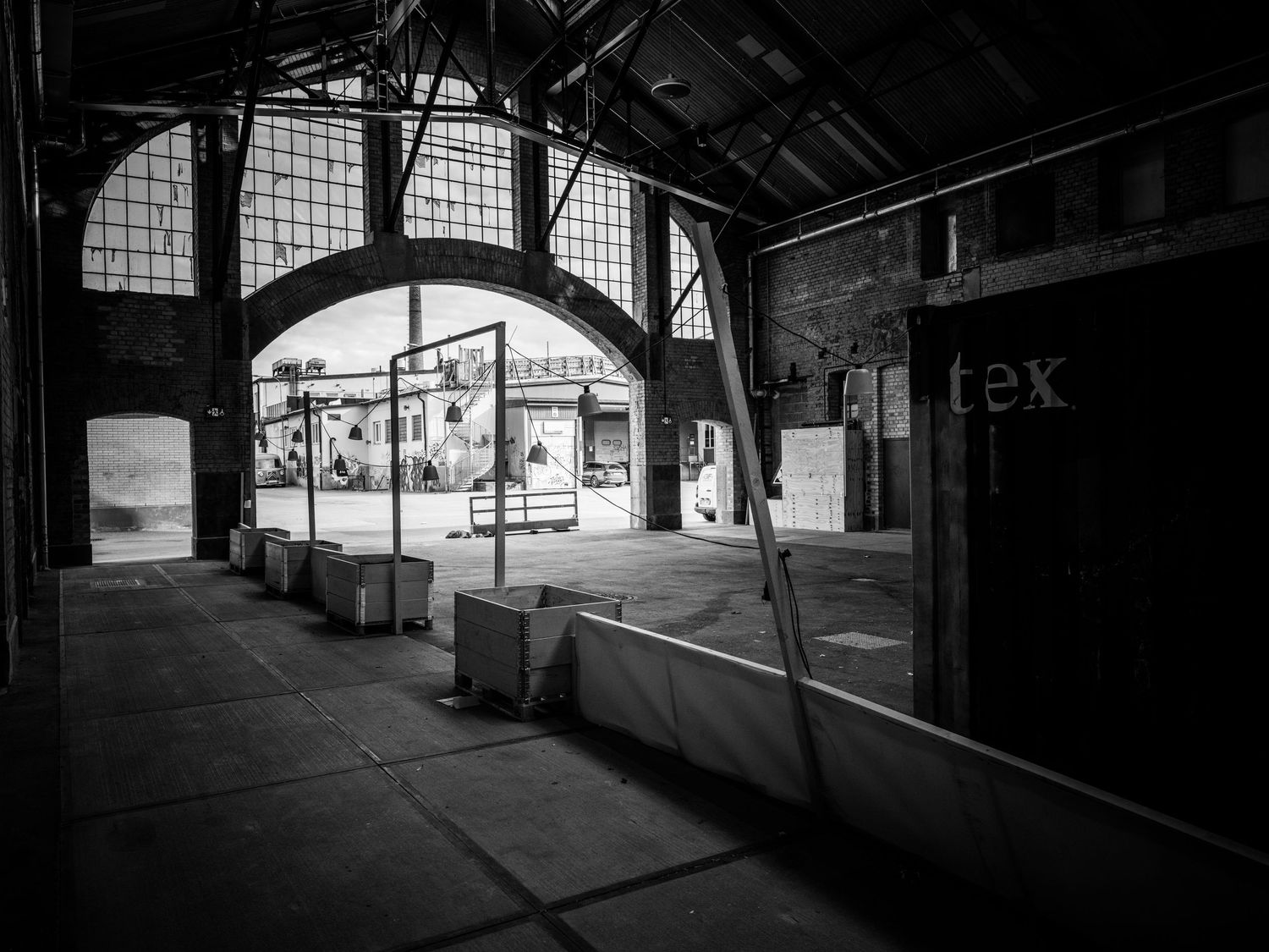Black and white interior of an industrial warehouse with arched opening and scattered equipment.