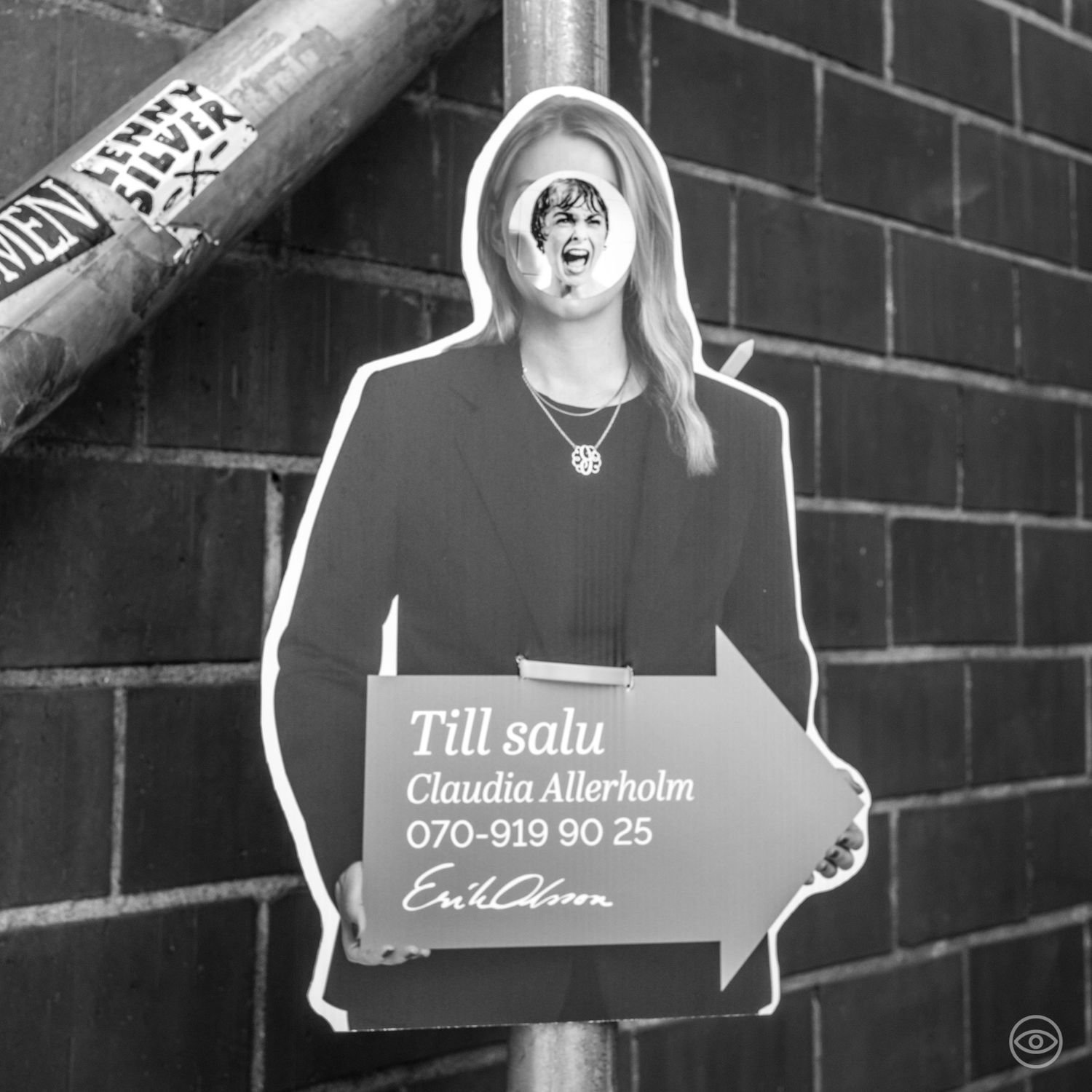 Cardboard cutout of a woman holding a real estate sign for Claudia Allerholm against a brick wall.