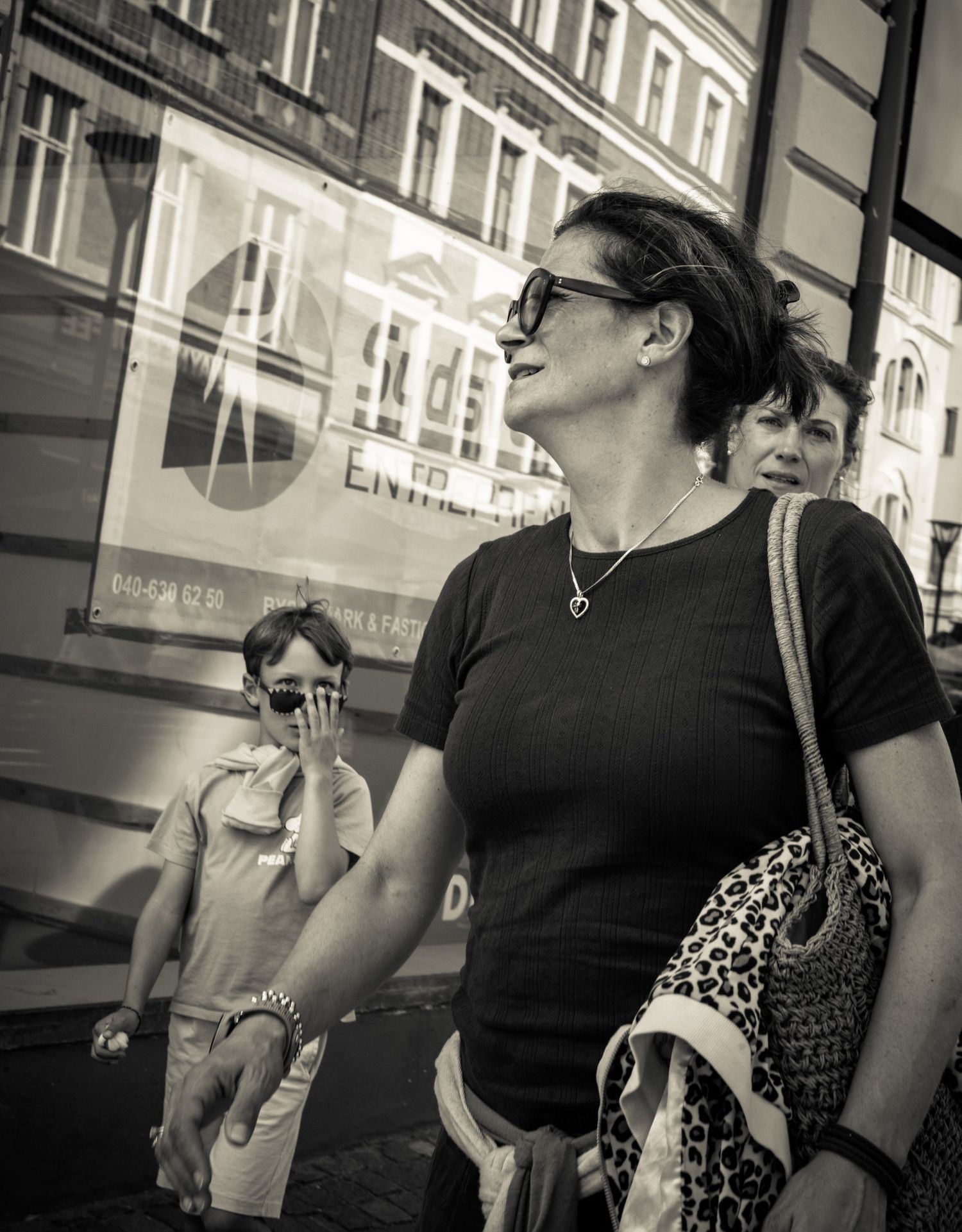 Dark-haired woman in sunglasses carries leopard print bag on busy urban street, black and white.