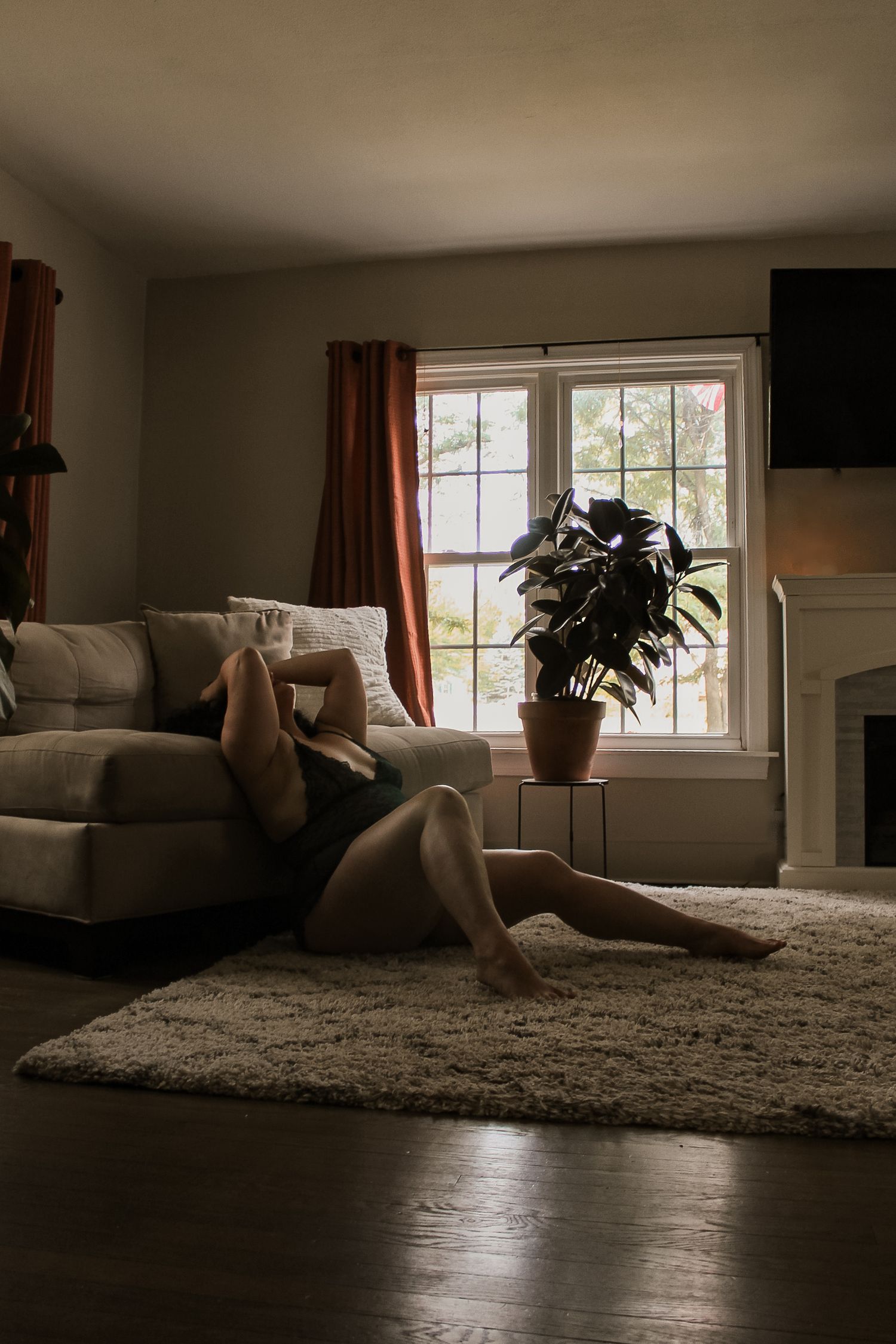 Woman relaxing on floor beside couch in dimly lit living room. Venus Boudoir by Candid House Studios, Syracuse, NY