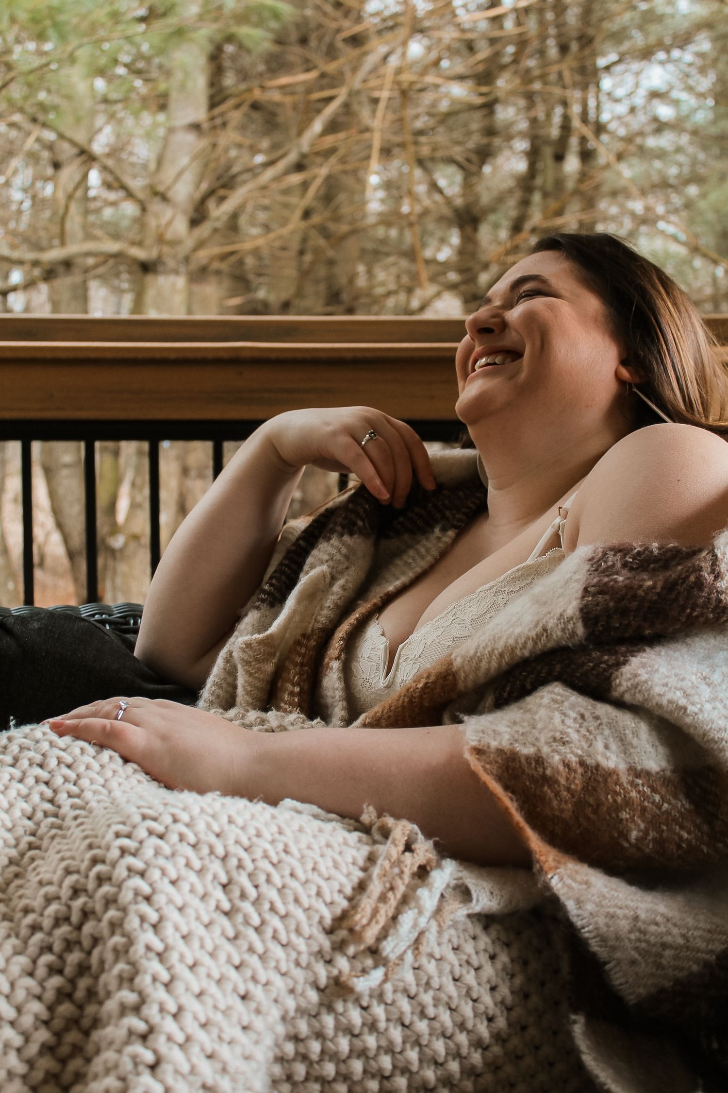 A smiling plus-size woman relaxes outdoors wrapped in cozy knit blankets on a deck chair.