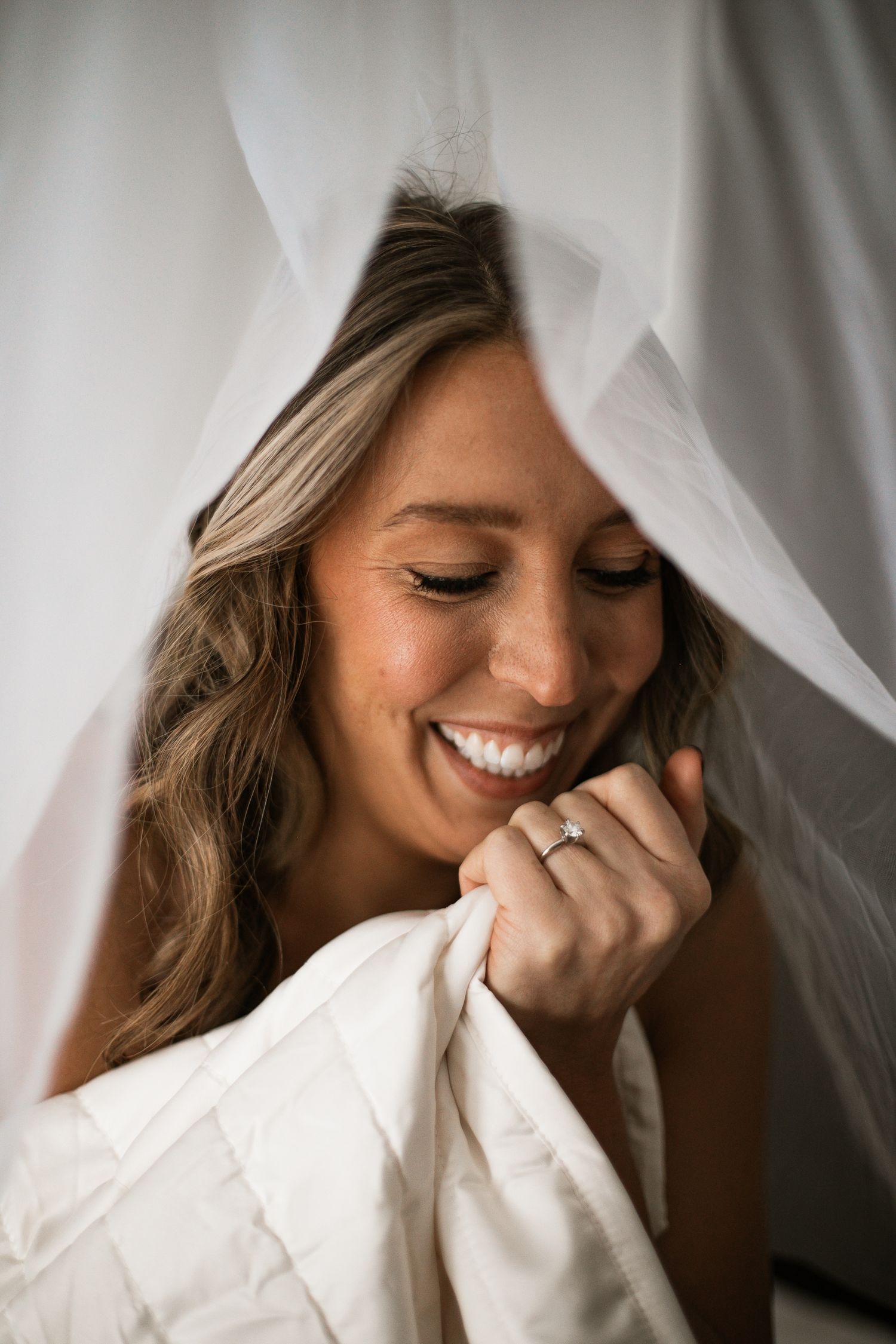 Smiling bride holding her veil and wedding dress, showcasing her diamond engagement ring on her wedding day.