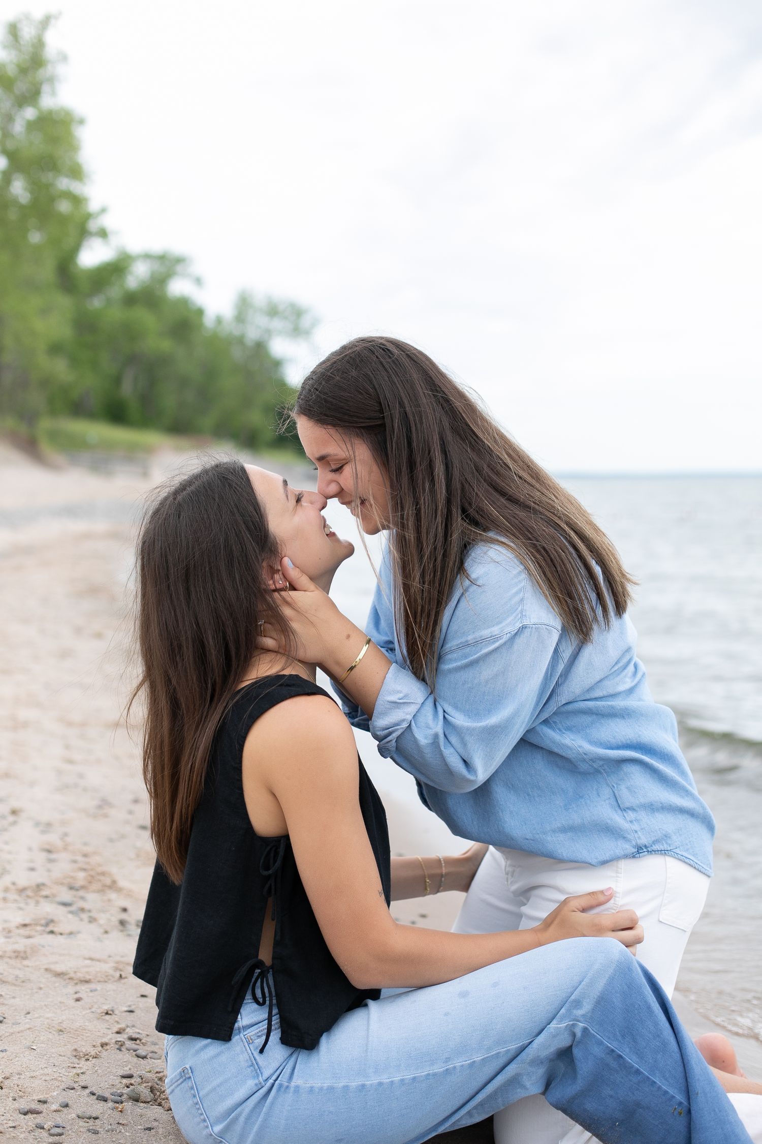 Two women share a romantic moment on a sandy beach, smiling and leaning in close together.