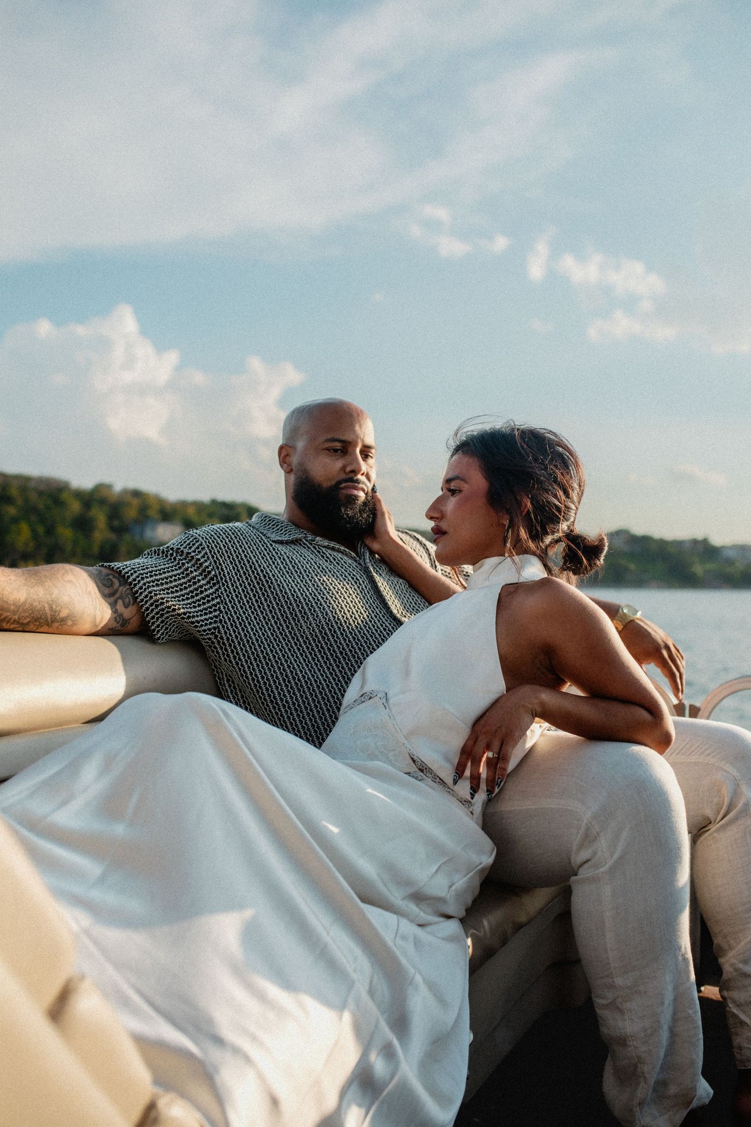 Couple relaxing together on luxury pontoon boat seating, gazing at each other with scenic lake backdrop.