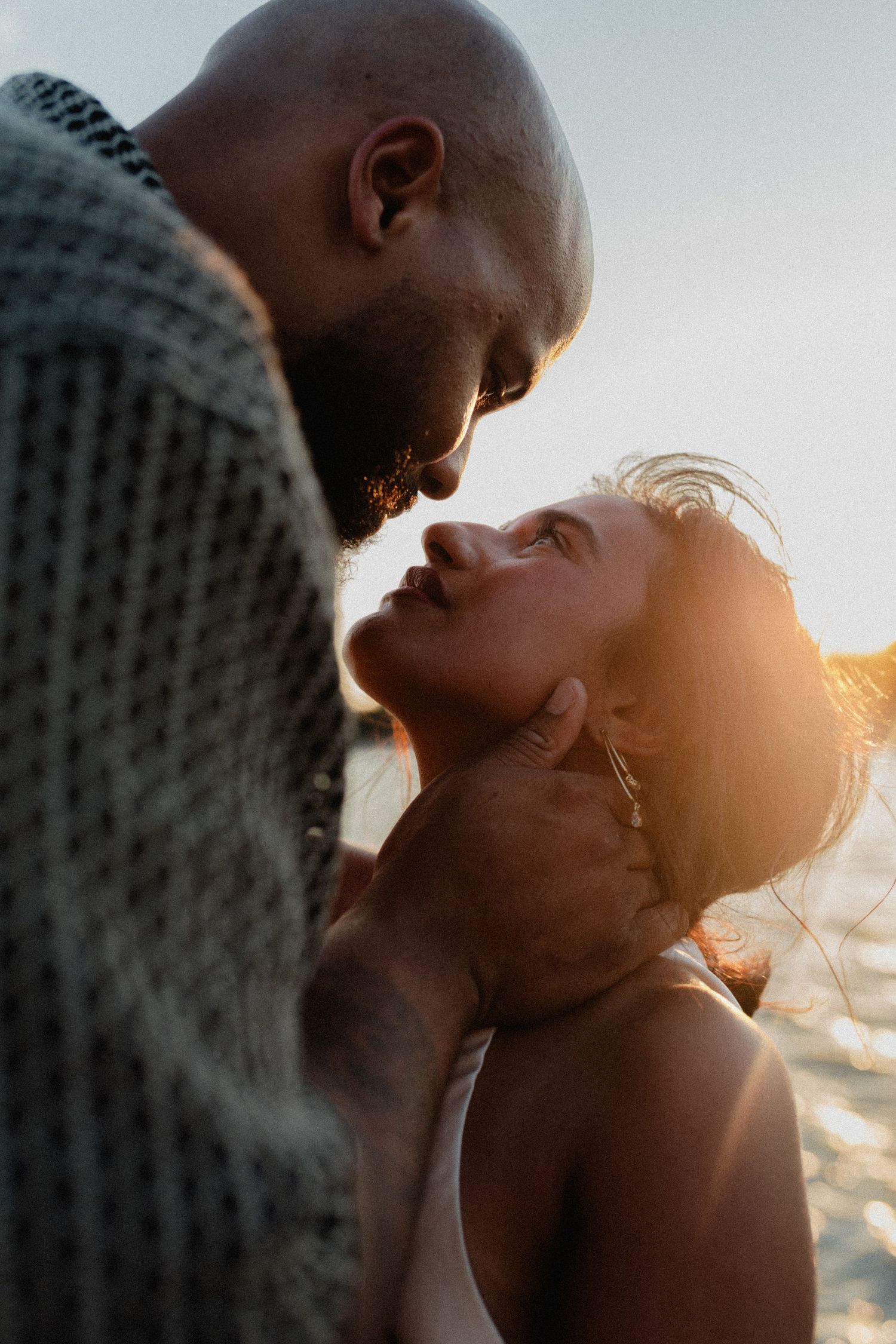 Romantic couple nearly kissing in golden sunset light, man gently cradling womans face outdoors.