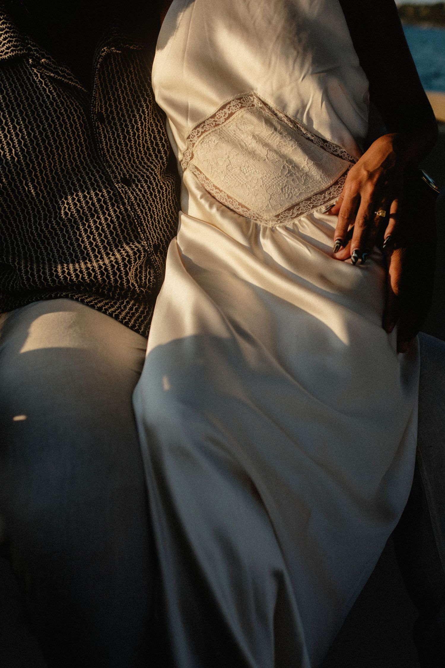 Close-up of woman in white satin dress with lace clutch bag sitting beside man in patterned shirt on boat.