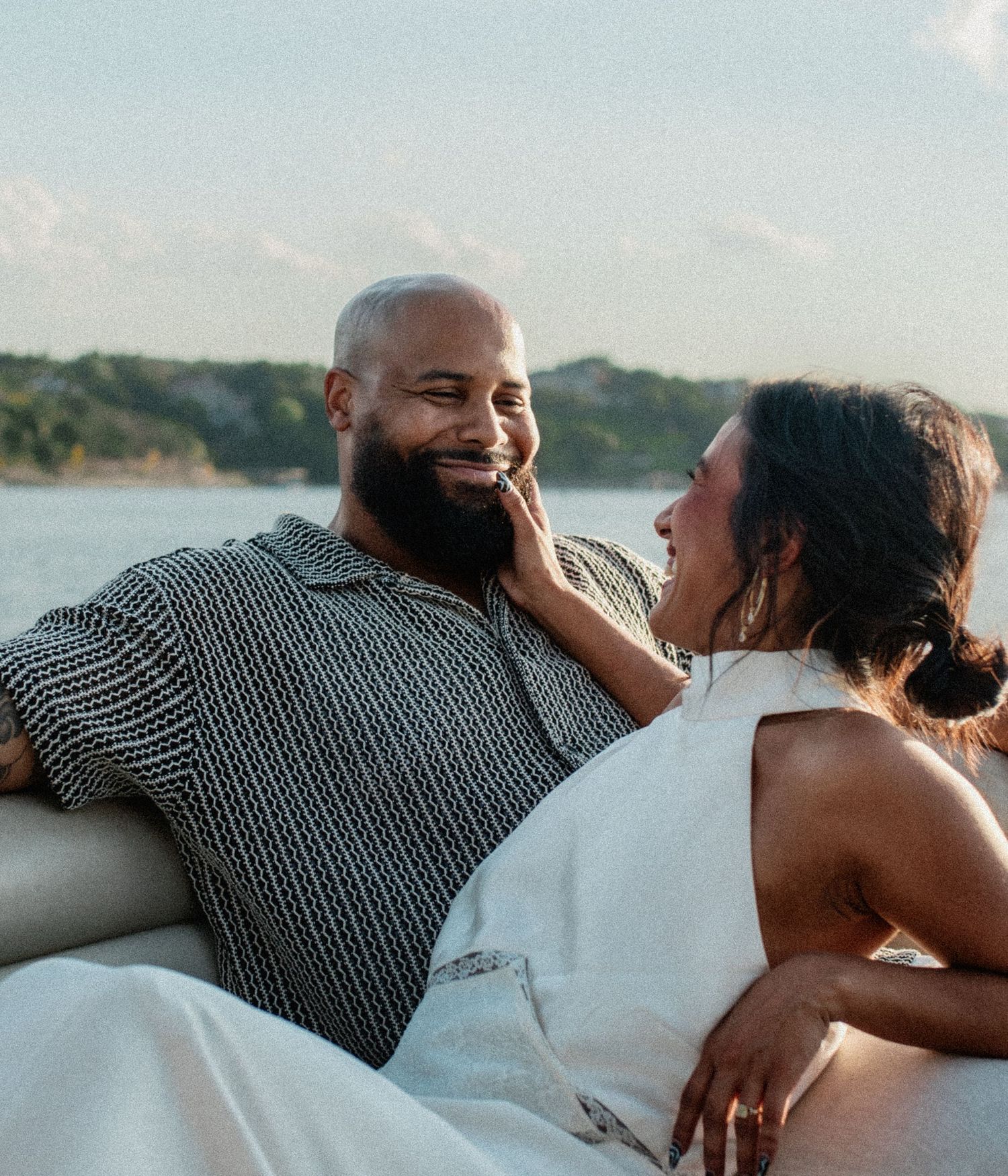 Happy couple laughing together on a boat, man with beard smiling as woman touches his face tenderly.