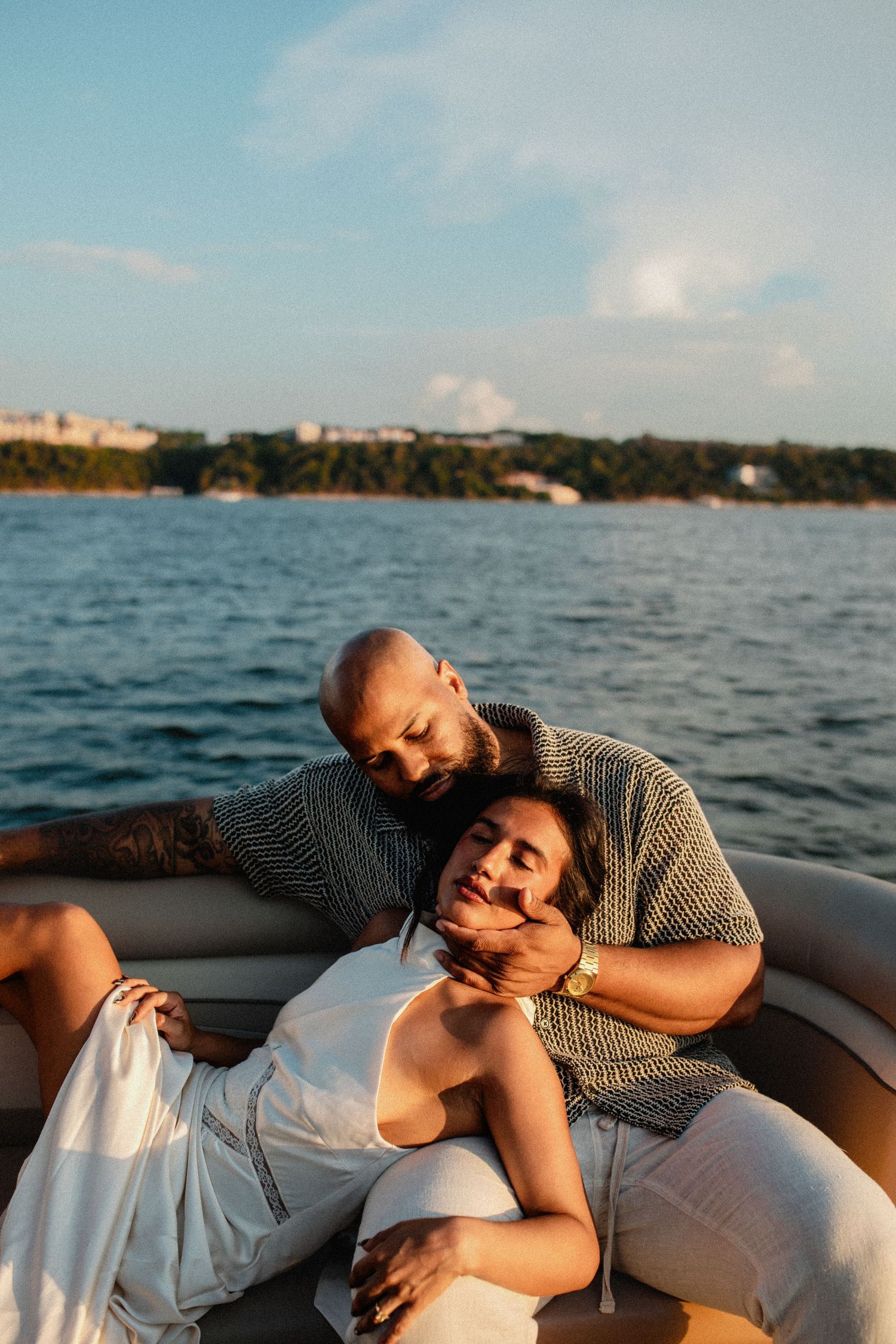 Couple cuddling on boat seat, man embracing woman from behind with ocean and blue sky backdrop.