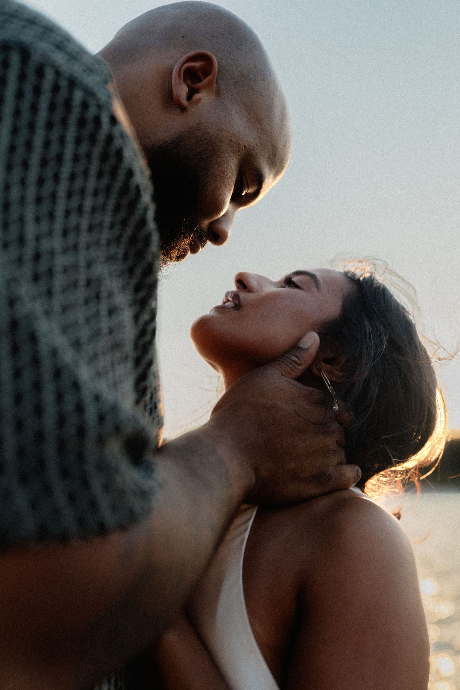 Intimate close-up of couple about to kiss, man tenderly holding womans face near water at dusk.