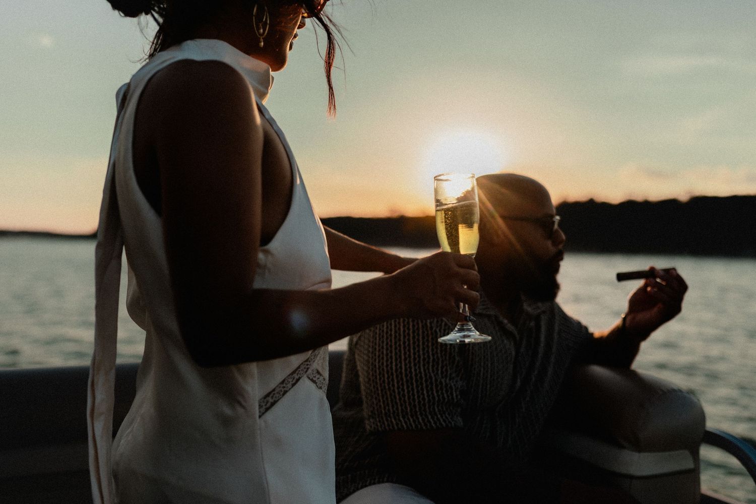 Couple enjoying sunset on boat, woman holding champagne glass, man relaxing nearby.